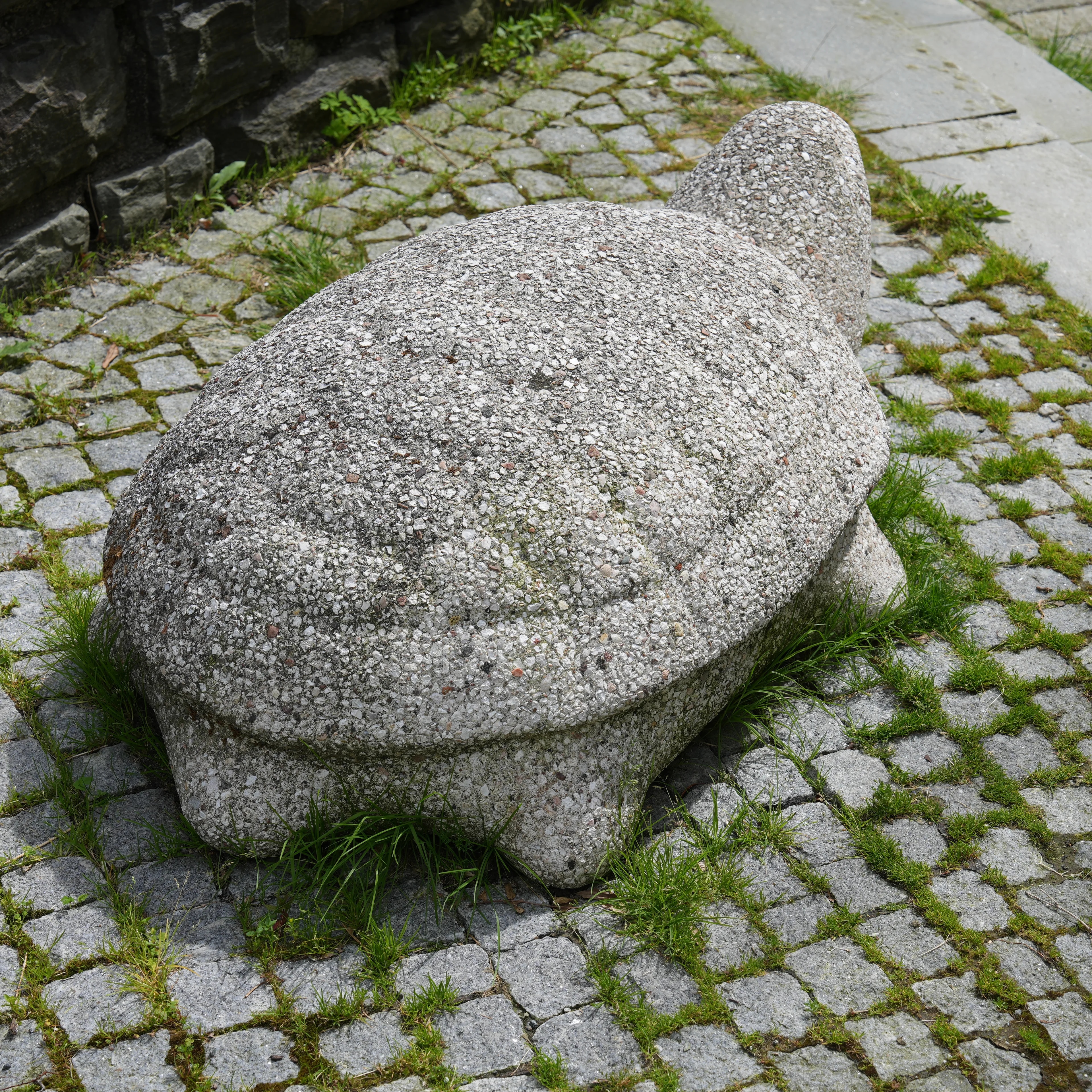 En steinskulptur formet som en skilpadde står på et underlag av brostein.