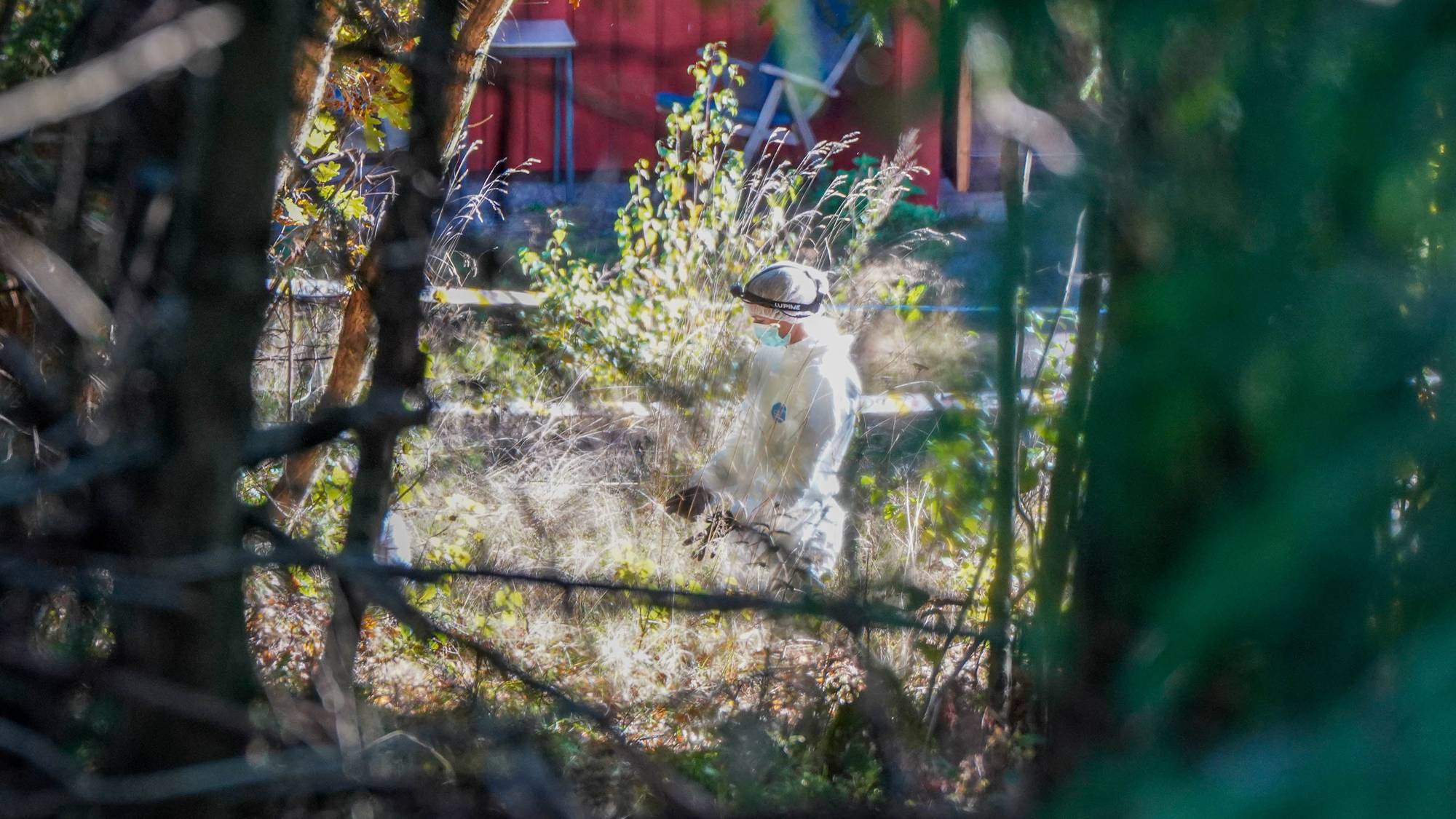 En person i beskyttelsesdrakt står i terrenget mellom en skog og en bolig.