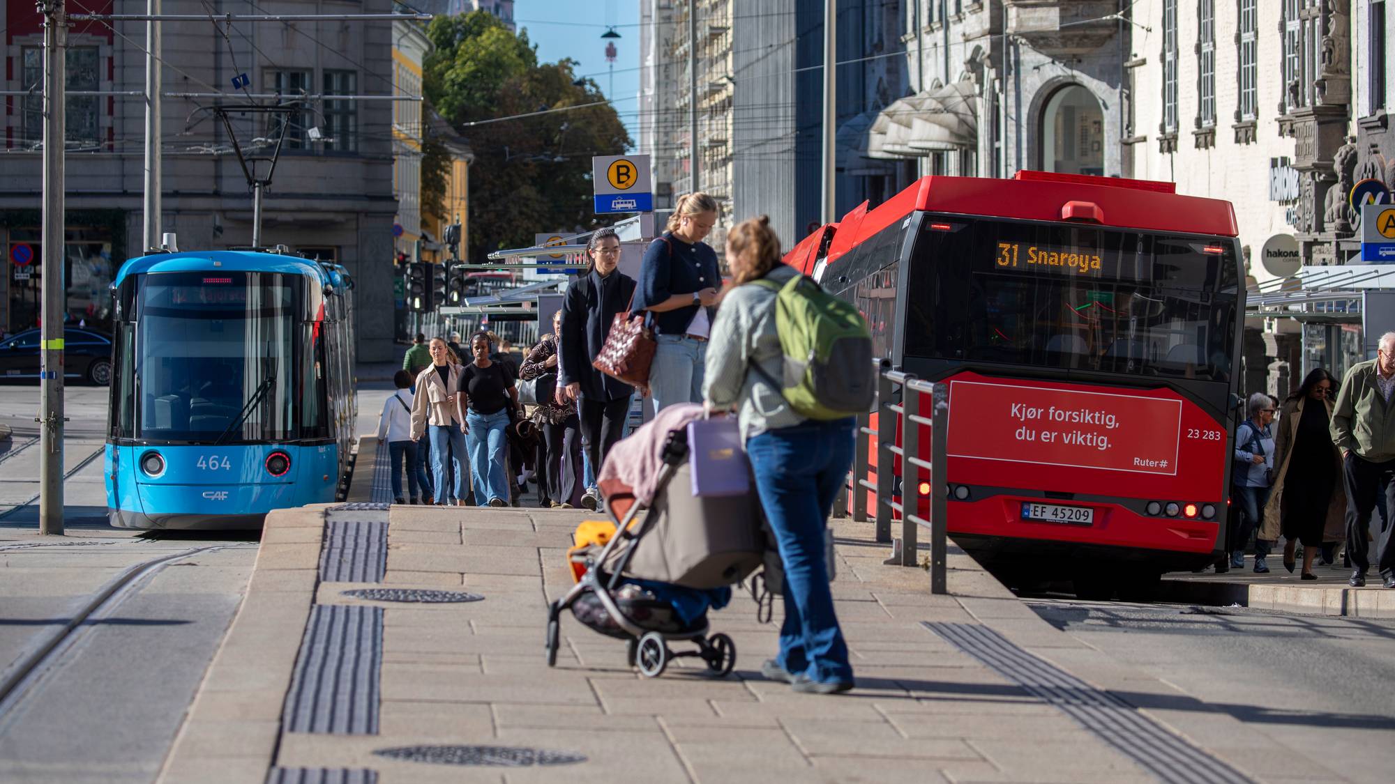 Fotgjengere ved et busstopp i Oslo sentrum med en trikk og en buss i bakgrunnen. (Bildebeskrivelsen er laget av en KI-tjeneste)