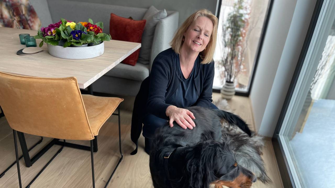 Unni Sandøy sitter på huk på gulvet og klapper hunden sin.