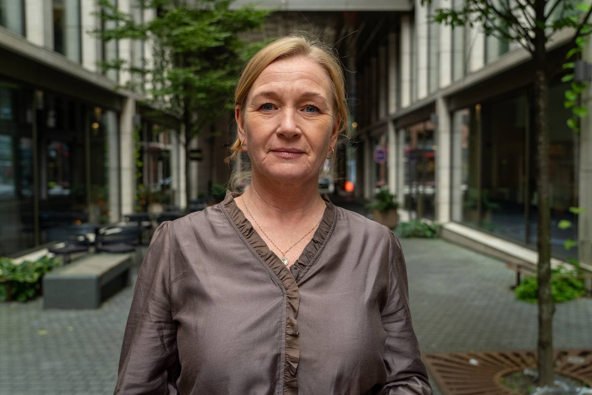 Kvinne står i en bygate med moderne arkitektur og ser mot kamera. (Bildebeskrivelsen er laget av en KI-tjeneste)