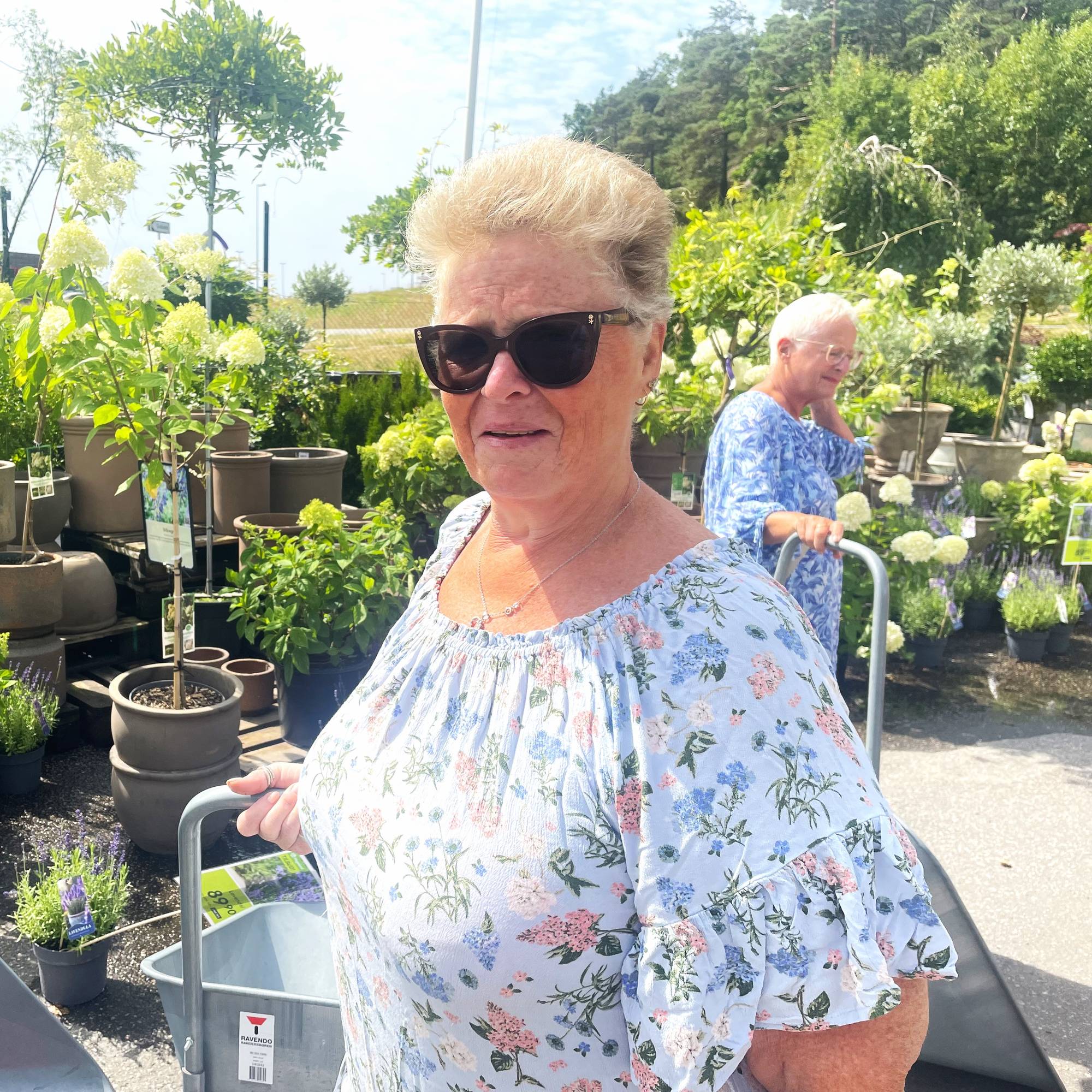 En dame med solbriller står foran blomster