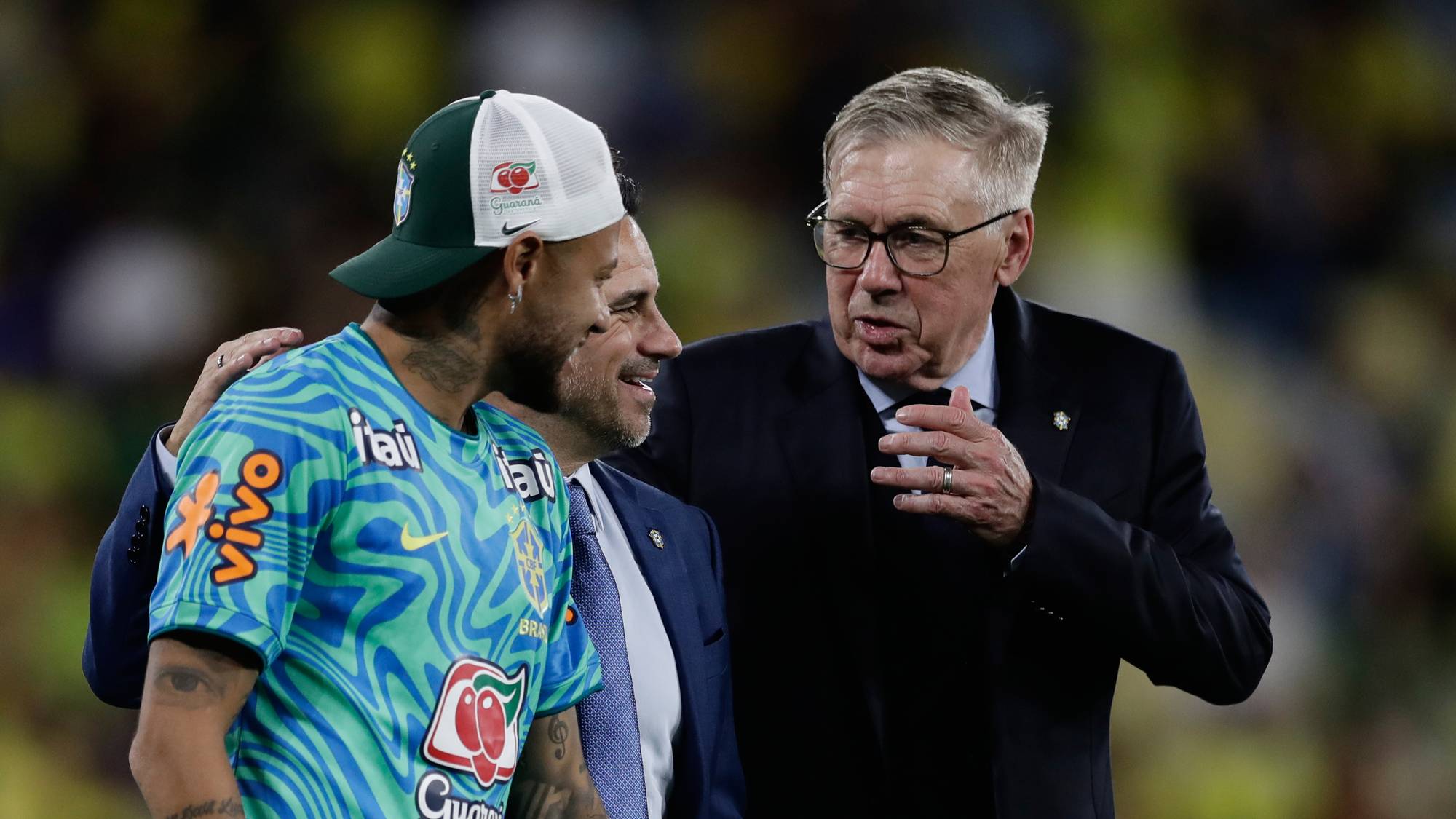 Fotballspilleren Neymar og trener Carlo Ancelotti snakker sammen. Neymar har på seg Brasils fotballtrøye og en caps. Ancelotti er kledd i dress. (Bildebeskrivelsen er laget av en KI-tjeneste)