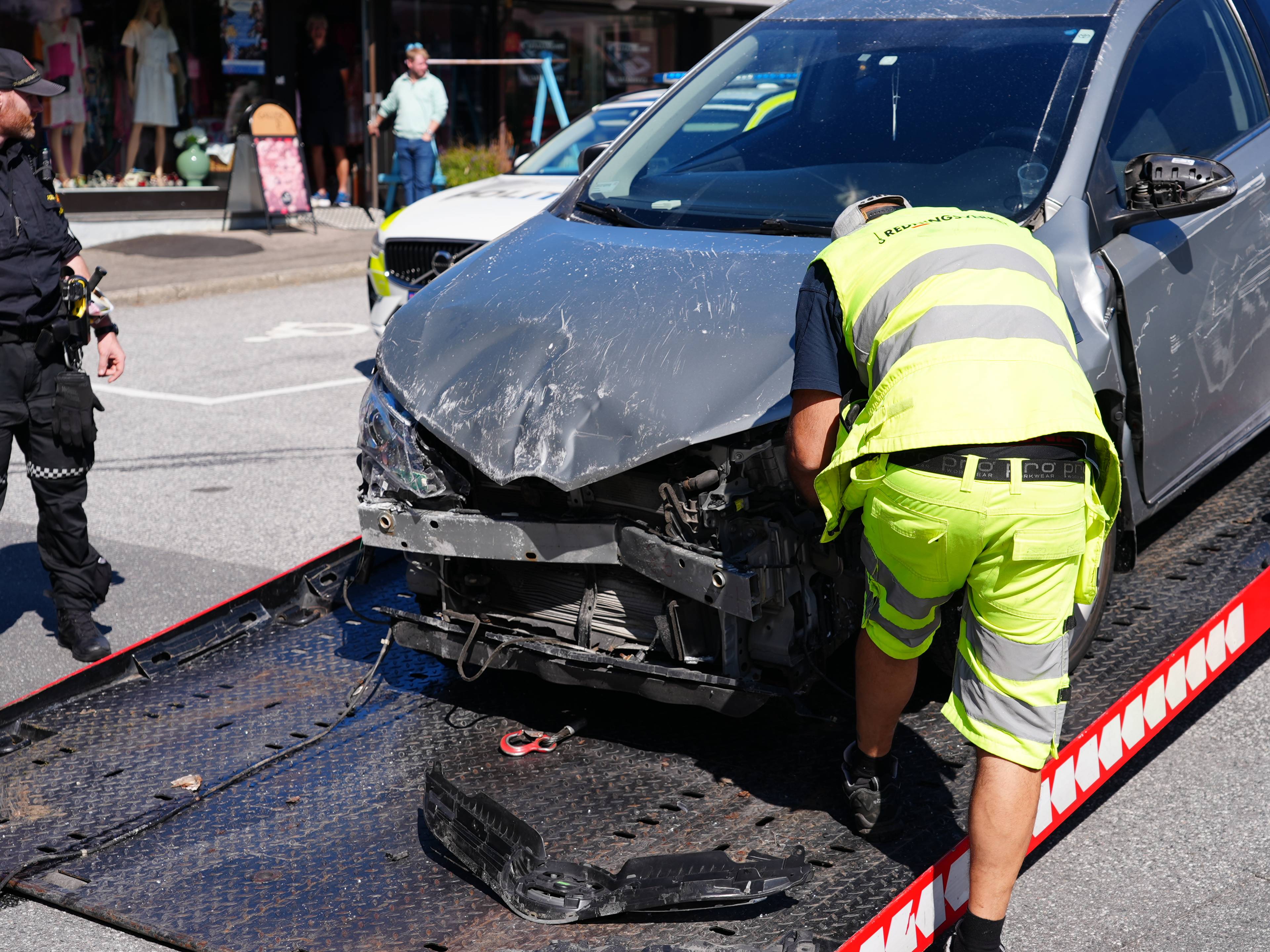 Bilberger laster opp en skadet personbil mens politi står ved siden av. (Bildebeskrivelsen er laget av en KI-tjeneste)