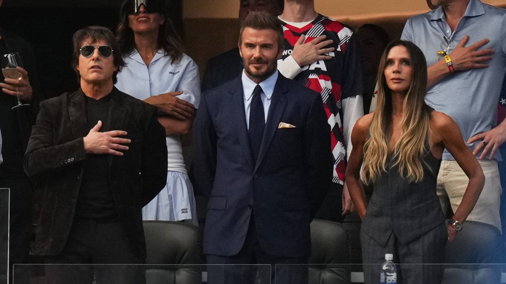 Tom Cruise, David Beckham og Victoria Beckham sitter på tribunen. De ser ut til å være under en nasjonalsang. Bildet er tatt fra en idrettsarena. (Bildebeskrivelsen er laget av en KI-tjeneste)