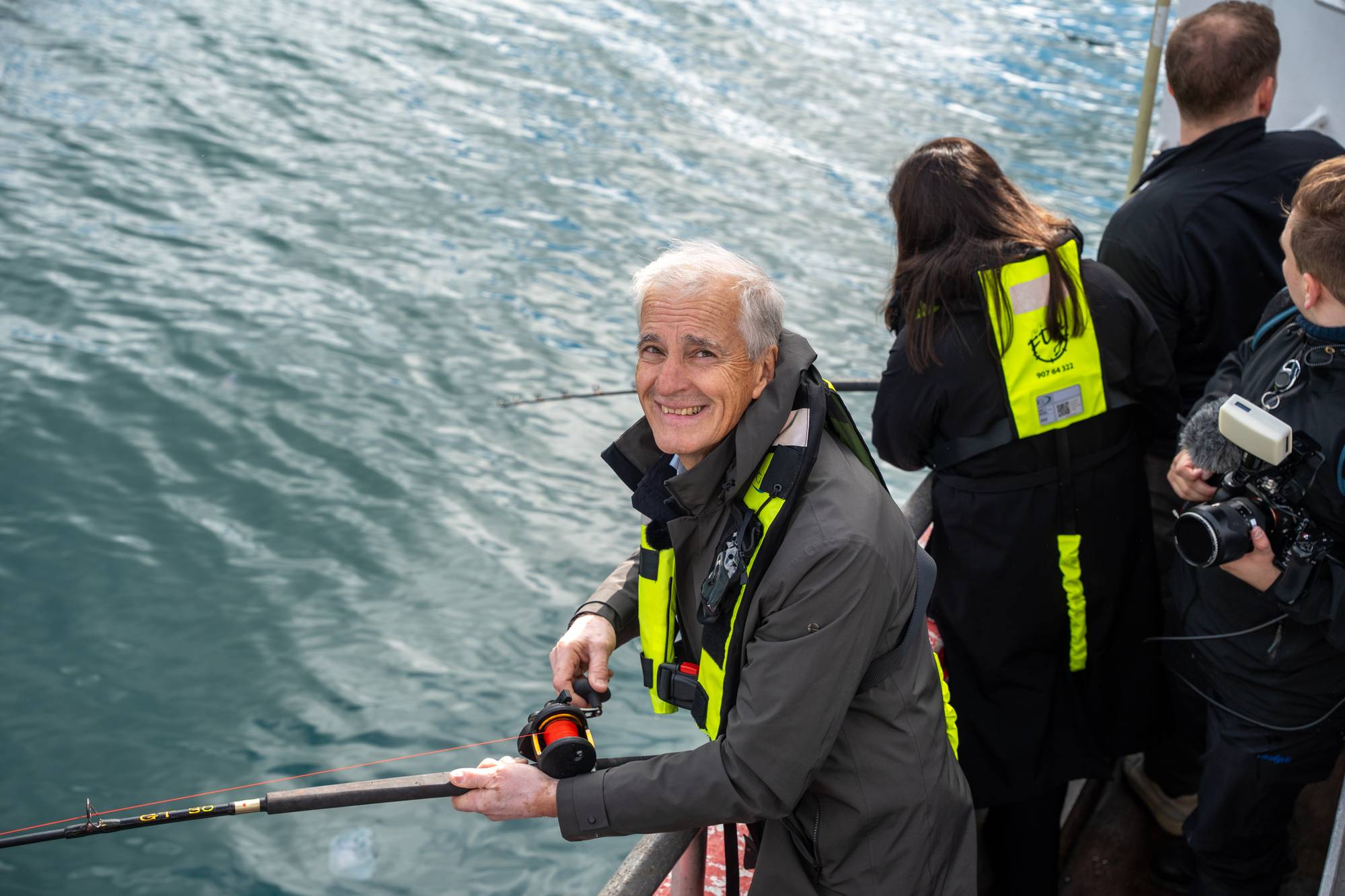 Statsminister Støre fisker fra en båt, med et smil om munnen.
