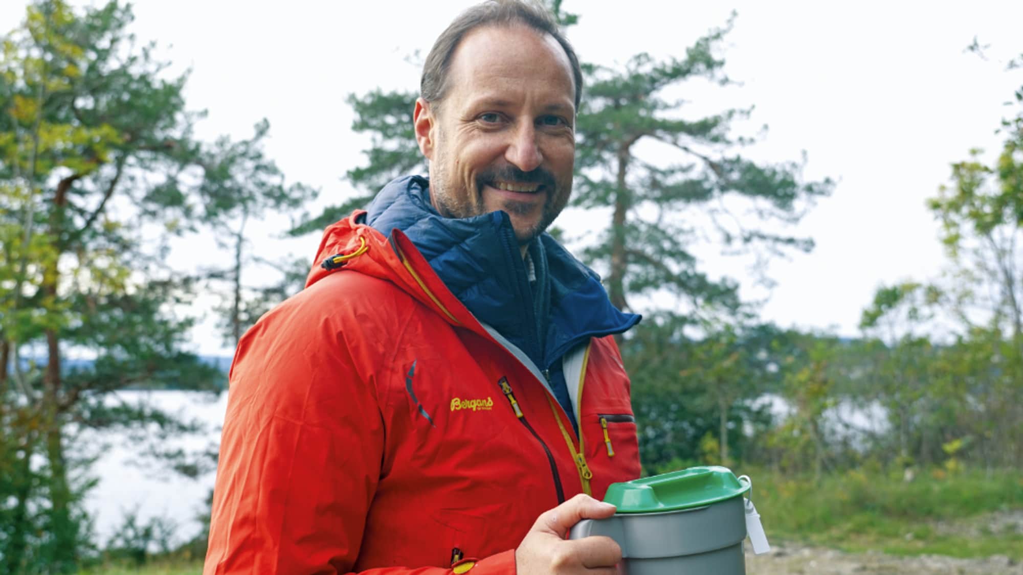 Kronprins Haakon i rød allværsjakke og med grønn TV-aksjonsbøsse
