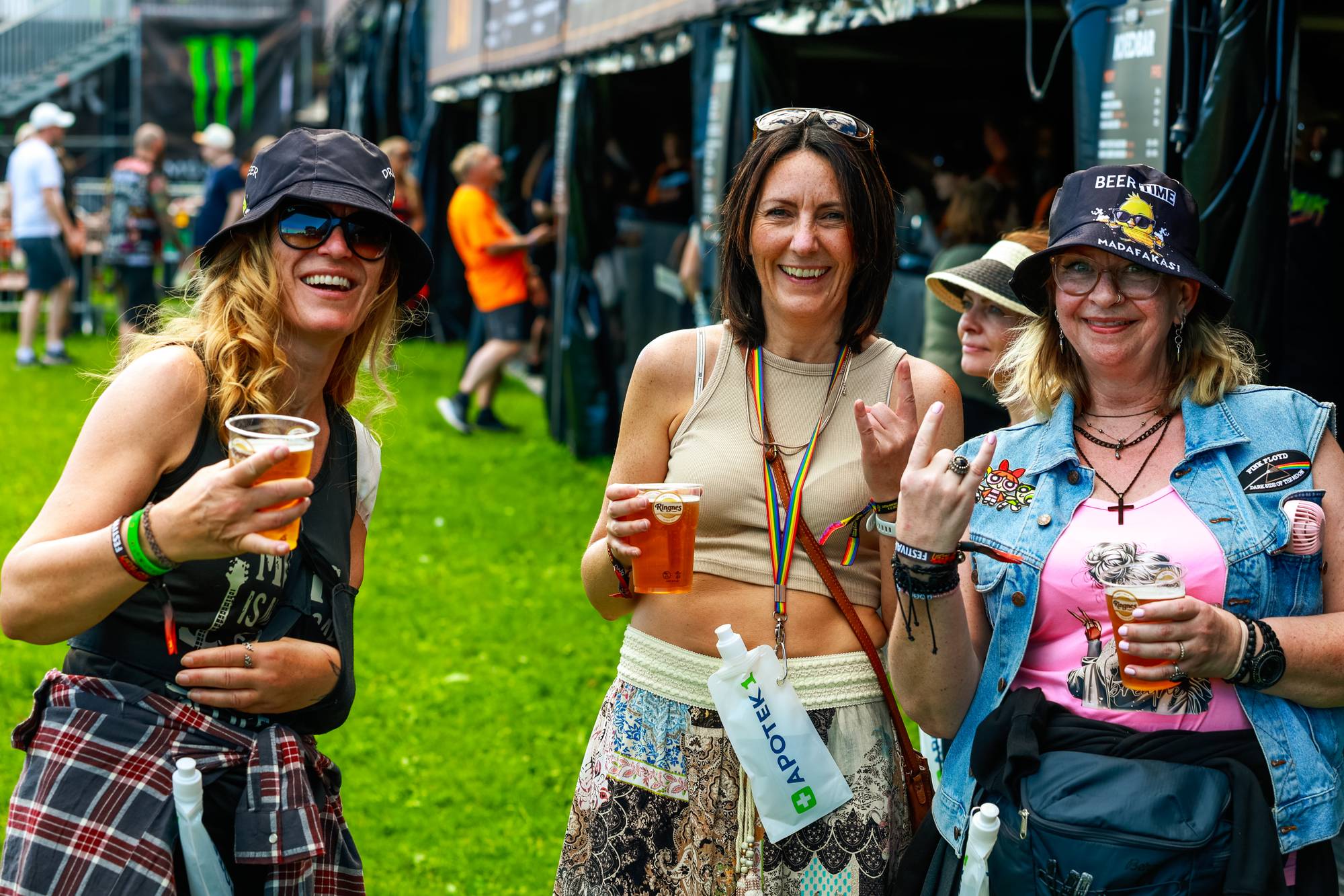 Tre kvinner under årets tons of rock-festival. De smiler og ser mot kamera. To av kvinnene holder opp hånden i et rocke-symbol. I bakgrunnen sees andre festivalgjengere og telt. (Bildebeskrivelsen er laget av en KI-tjeneste)
