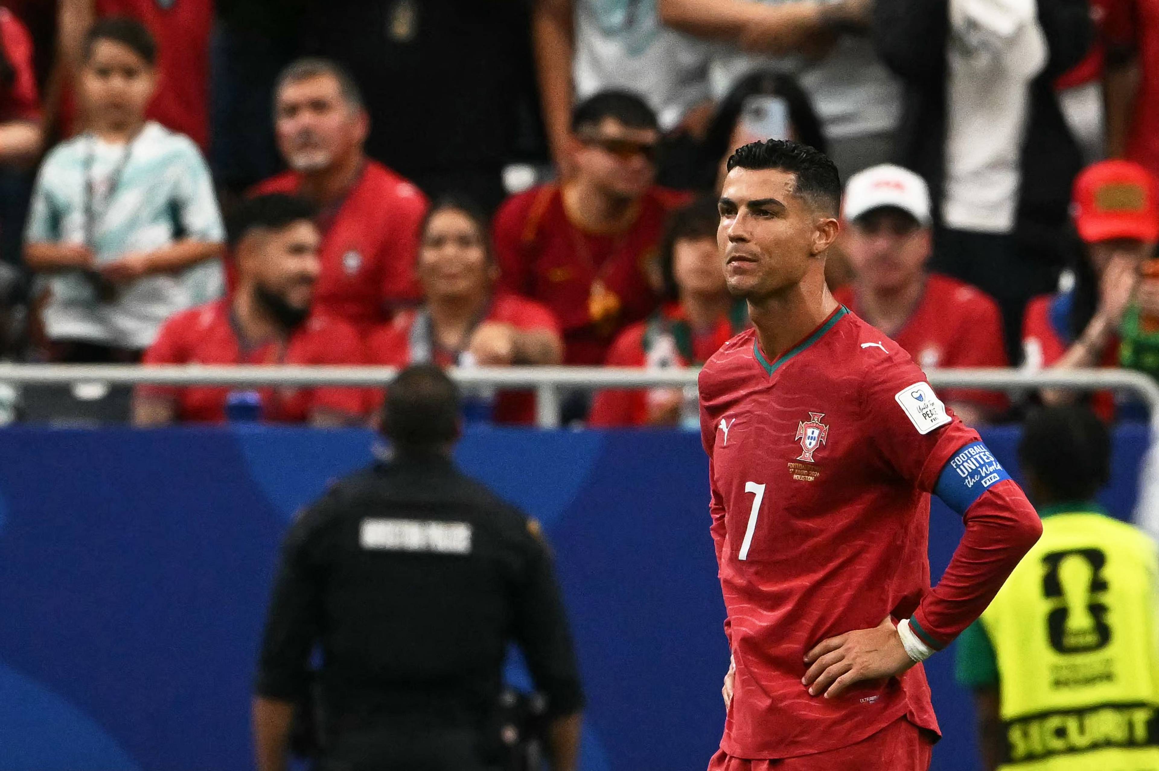 Cristiano Ronaldo i Portugal-drakt. Han står på en fotballbane. Publikum er i bakgrunnen. (Bildebeskrivelsen er laget av en KI-tjeneste)