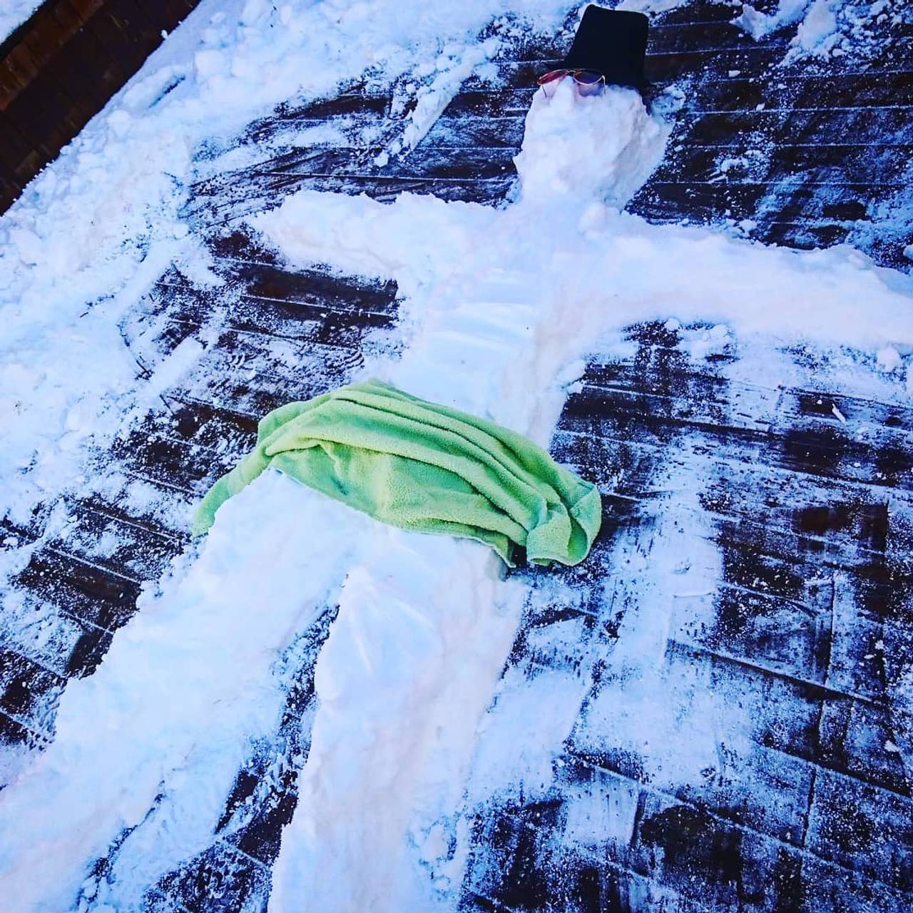 En liggende snømann, iført hatt og håndkle, på en terrasse.