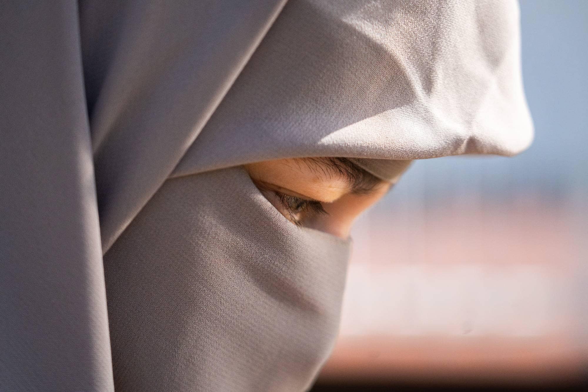 Et nærbilde av et øye på en person som bærer en hijab. Øyet er åpent og sett fra siden. Huden er lys og er delvis dekket av det grå stoffet til hijaben. (Bildebeskrivelsen er laget av en KI-tjeneste)