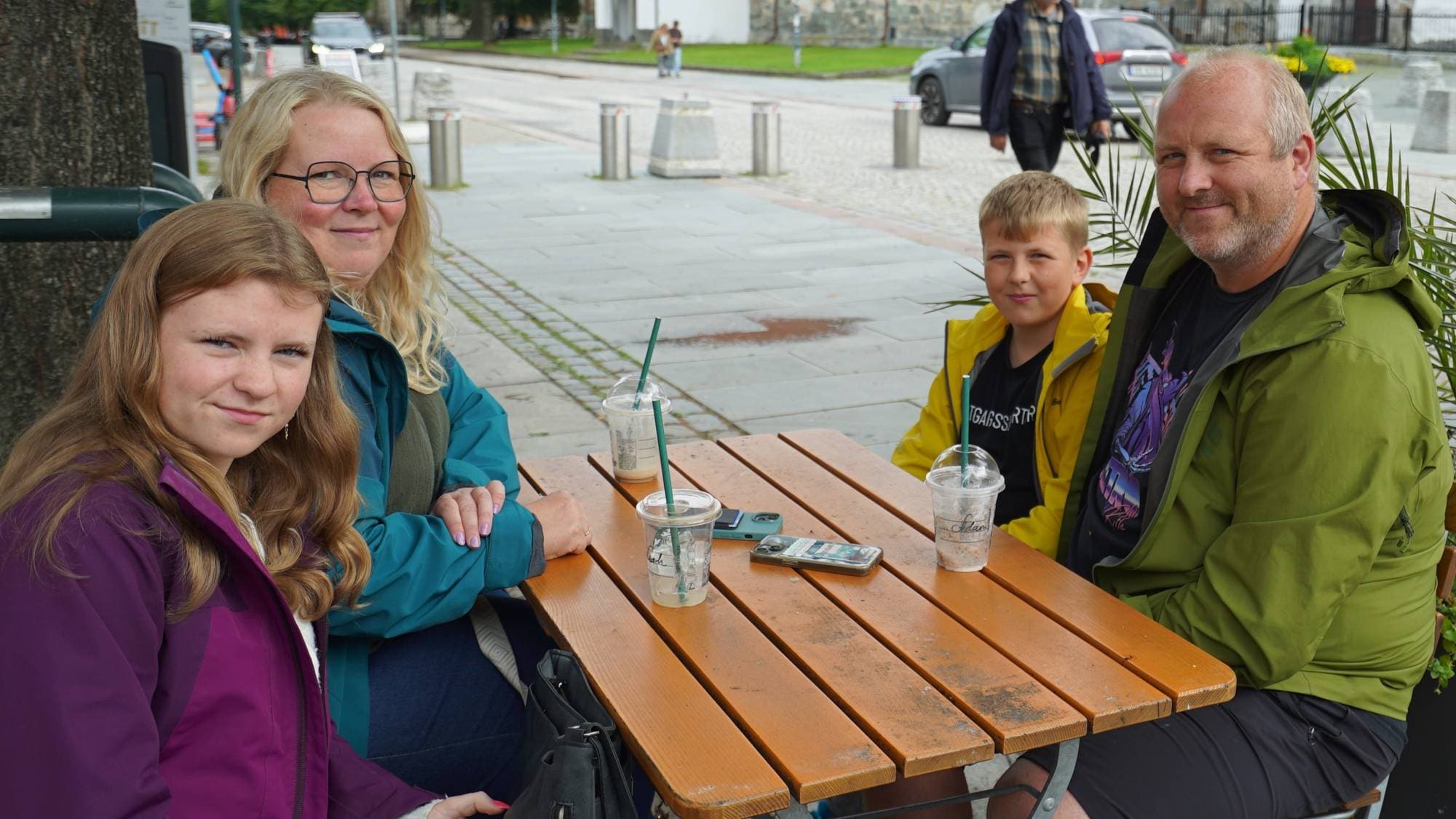 En familie sitter ute rundt et bord i Trondheim sentrum. Det er mor, datter, far og sønn.