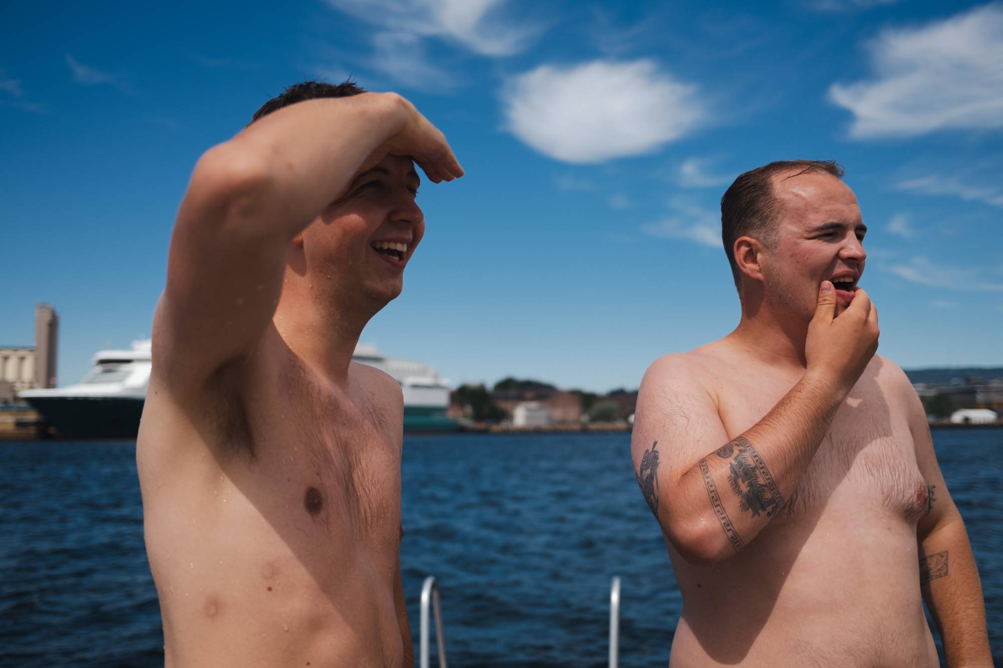 To menn står på en brygge. Bak dem ser man havet. De har badet. 