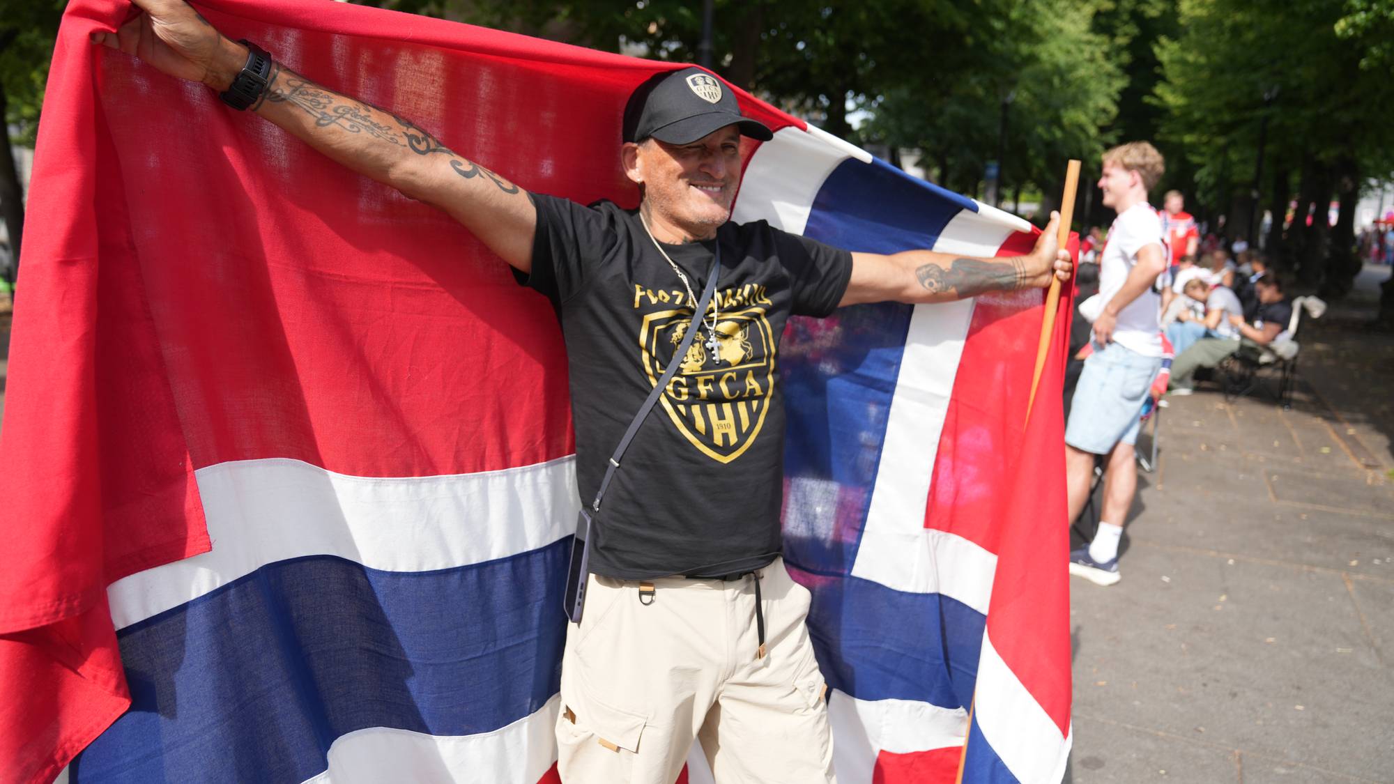Mann holder opp et stort norsk flagg utendørs. (Bildebeskrivelsen er laget av en KI-tjeneste)
