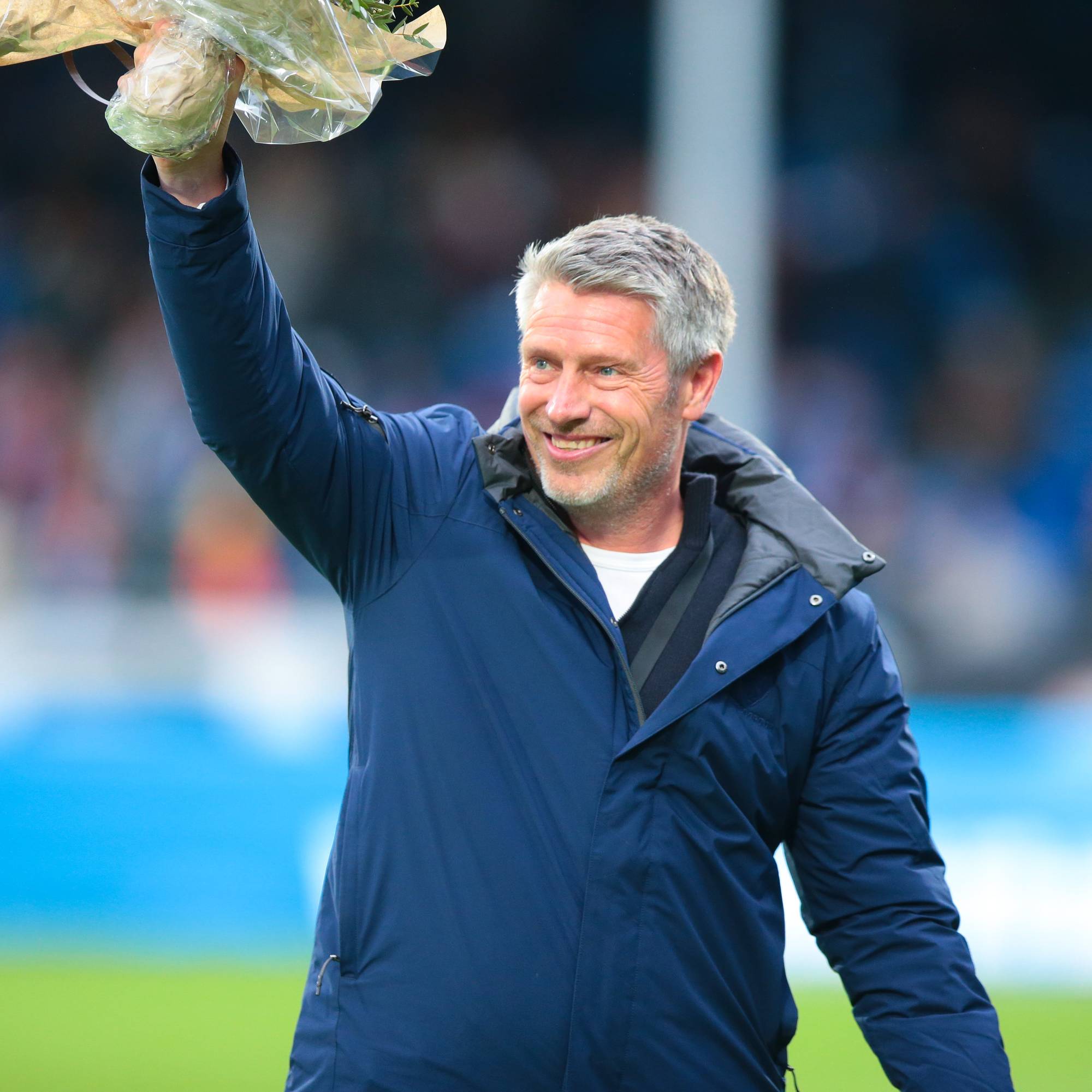 Kjetil Knutsen vinker med en blomsterbukett på en fotballbane. (Bildebeskrivelsen er laget av en KI-tjeneste)