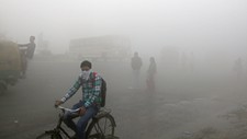 En mann på sykkel dekker ansiktet i den tykke smogen i New Delhi i India.