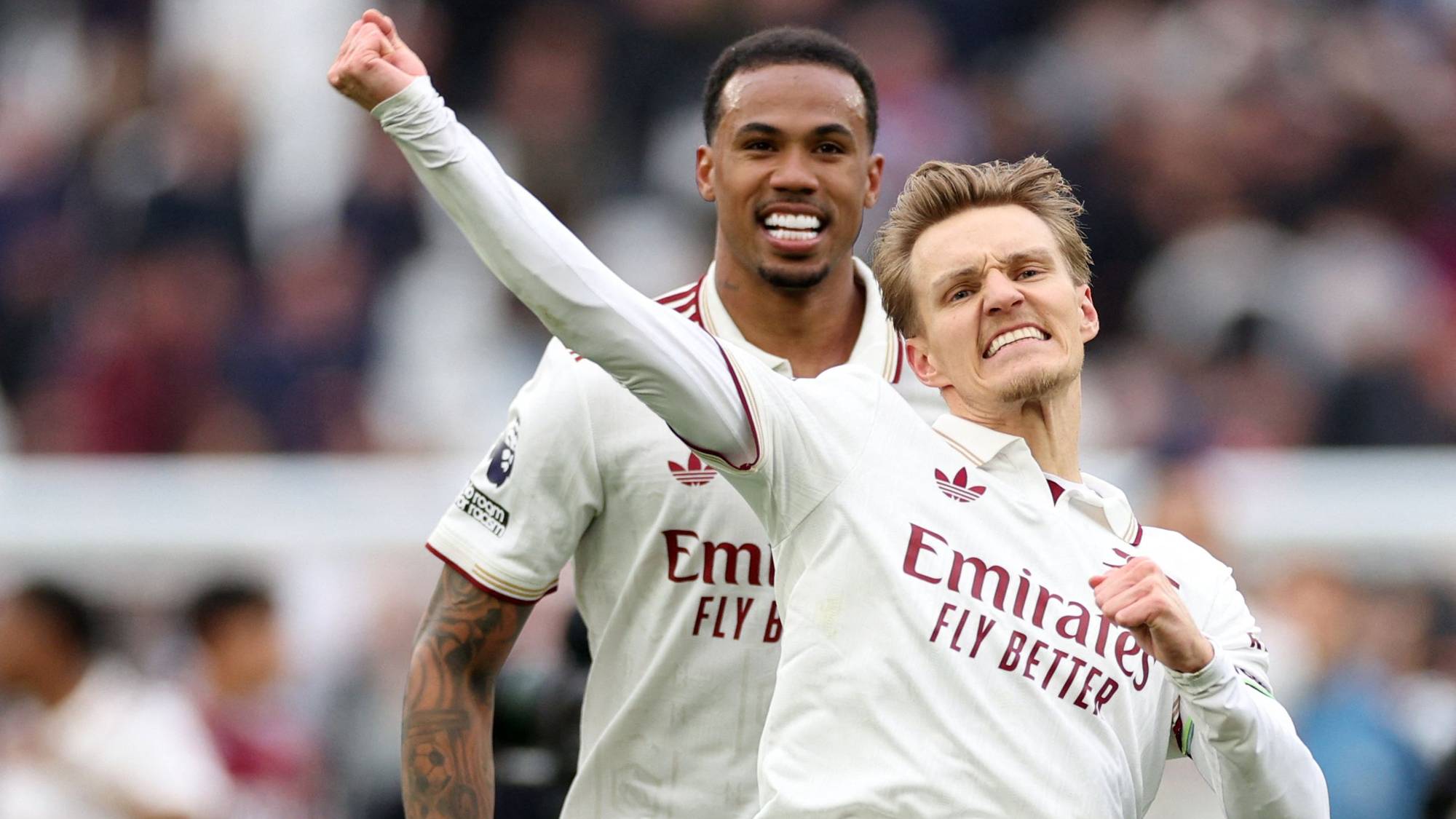 To fotballspillere i hvite drakt feirer. Den ene, Gabriel, smiler mens han ser bakover. Den andre, som ser fremover, har armen hevet i luften. (Bildebeskrivelsen er laget av en KI-tjeneste)