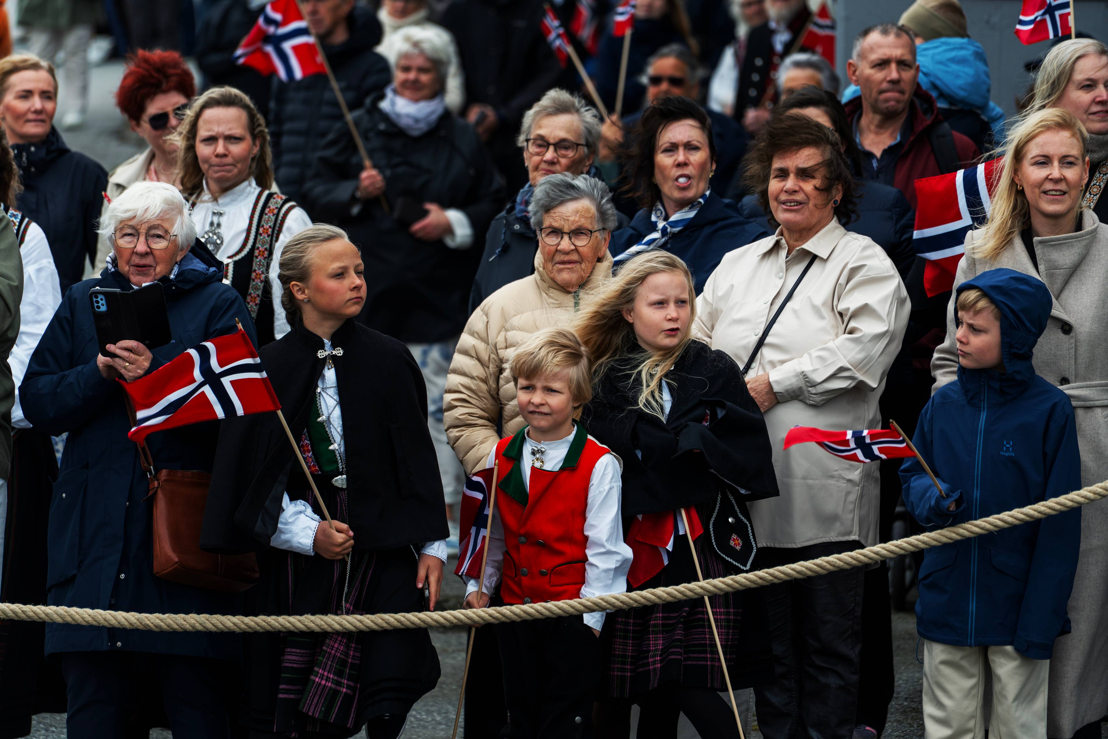 Barn og voksne står med vind i håret, holder norske flagg og venter på kongen.