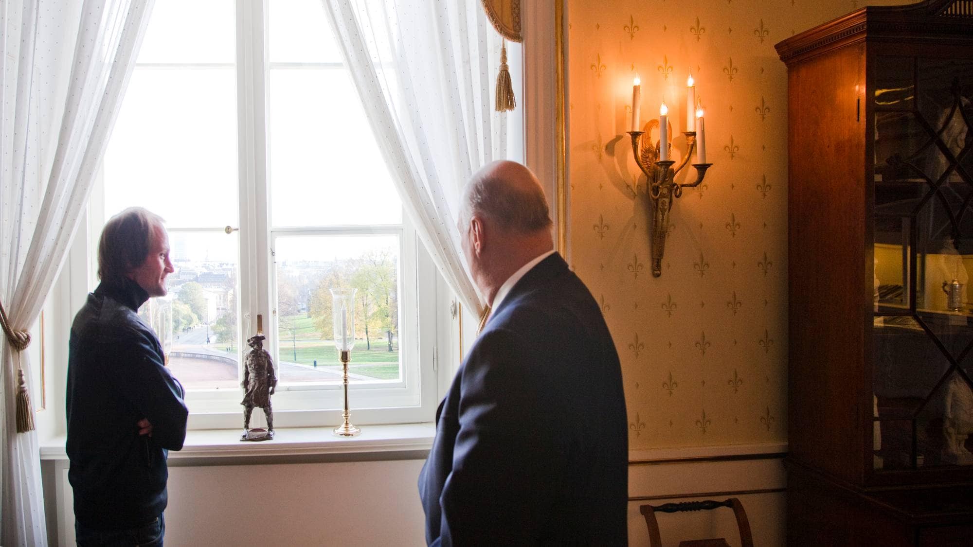 Christer Modin og kong Harald står foran et vindu på Slottet og ser ut mot Karl Johan