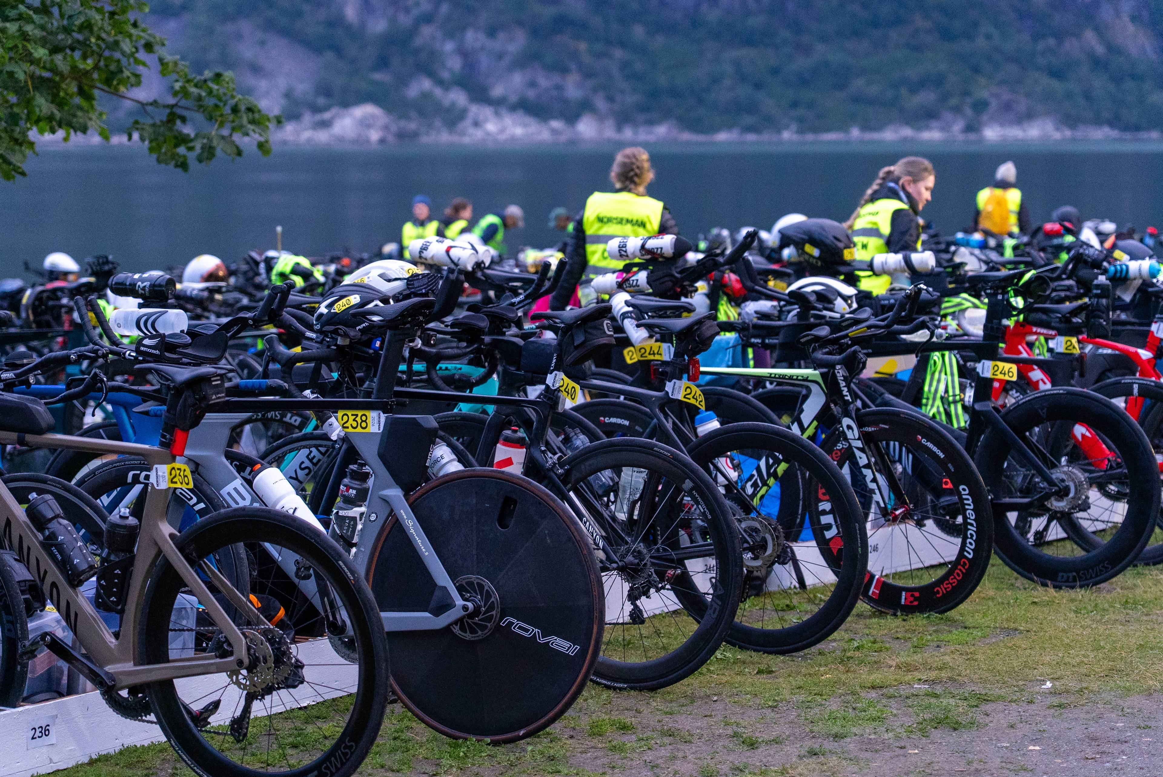 Mange sykler står oppstilt i skifterommet ved et vann før triatlonkonkurransen Norseman. (Bildebeskrivelsen er laget av en KI-tjeneste)