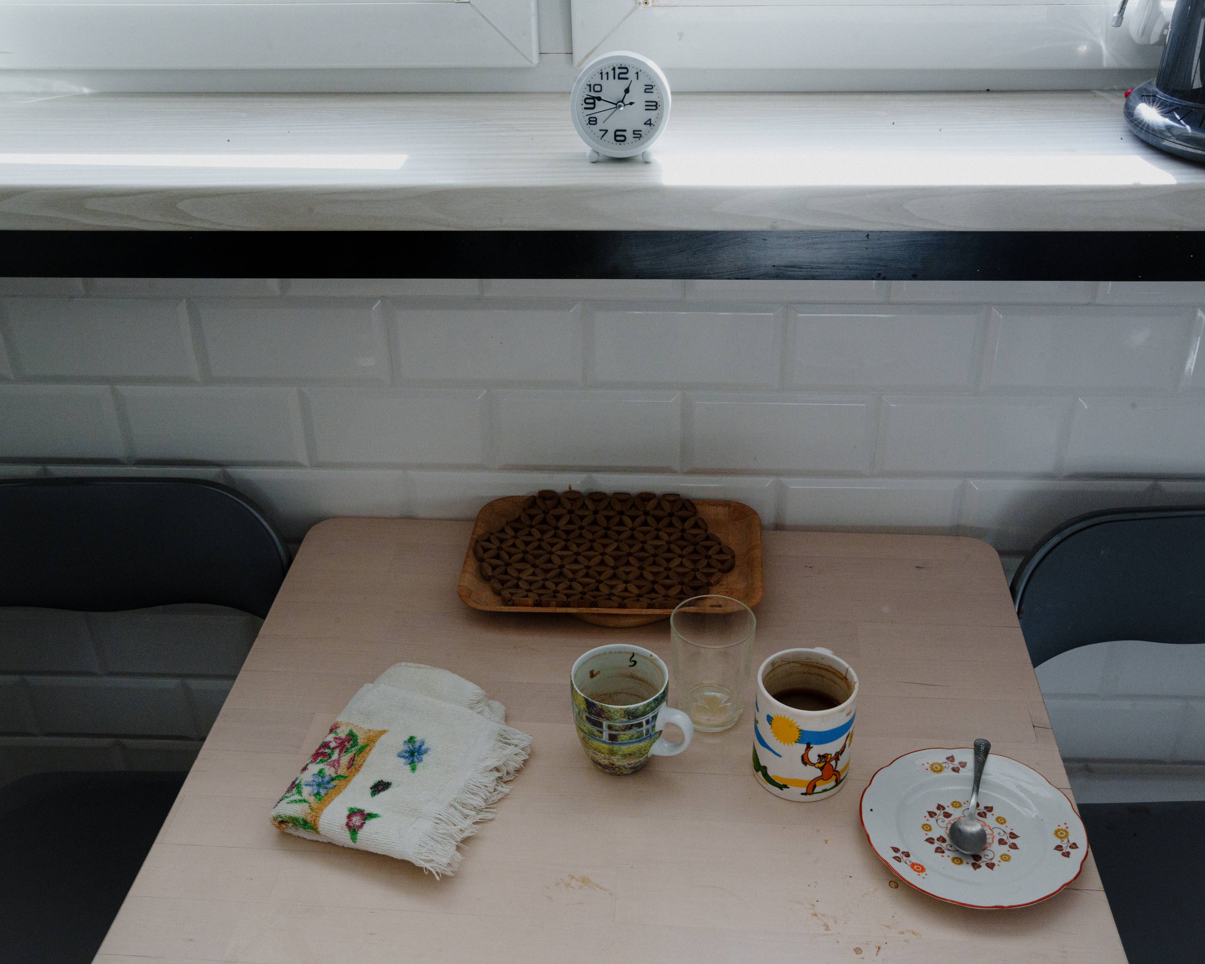 To kopper og et enkelt fat med noen små matrester står på et kjøkkenbord. Ved vinduet over treffer sollyset en liten klokke