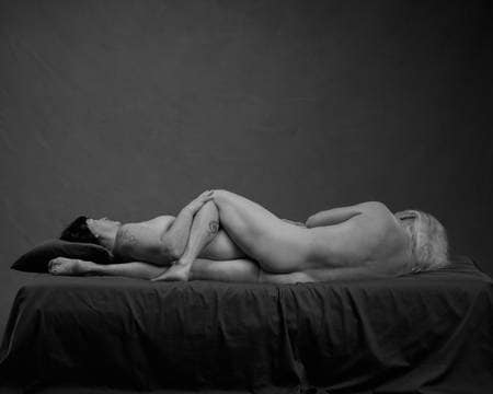 En naken dame ligger tett inntil en naken mann i senga. De har hue hver sin vei og ligger i omvendt skje