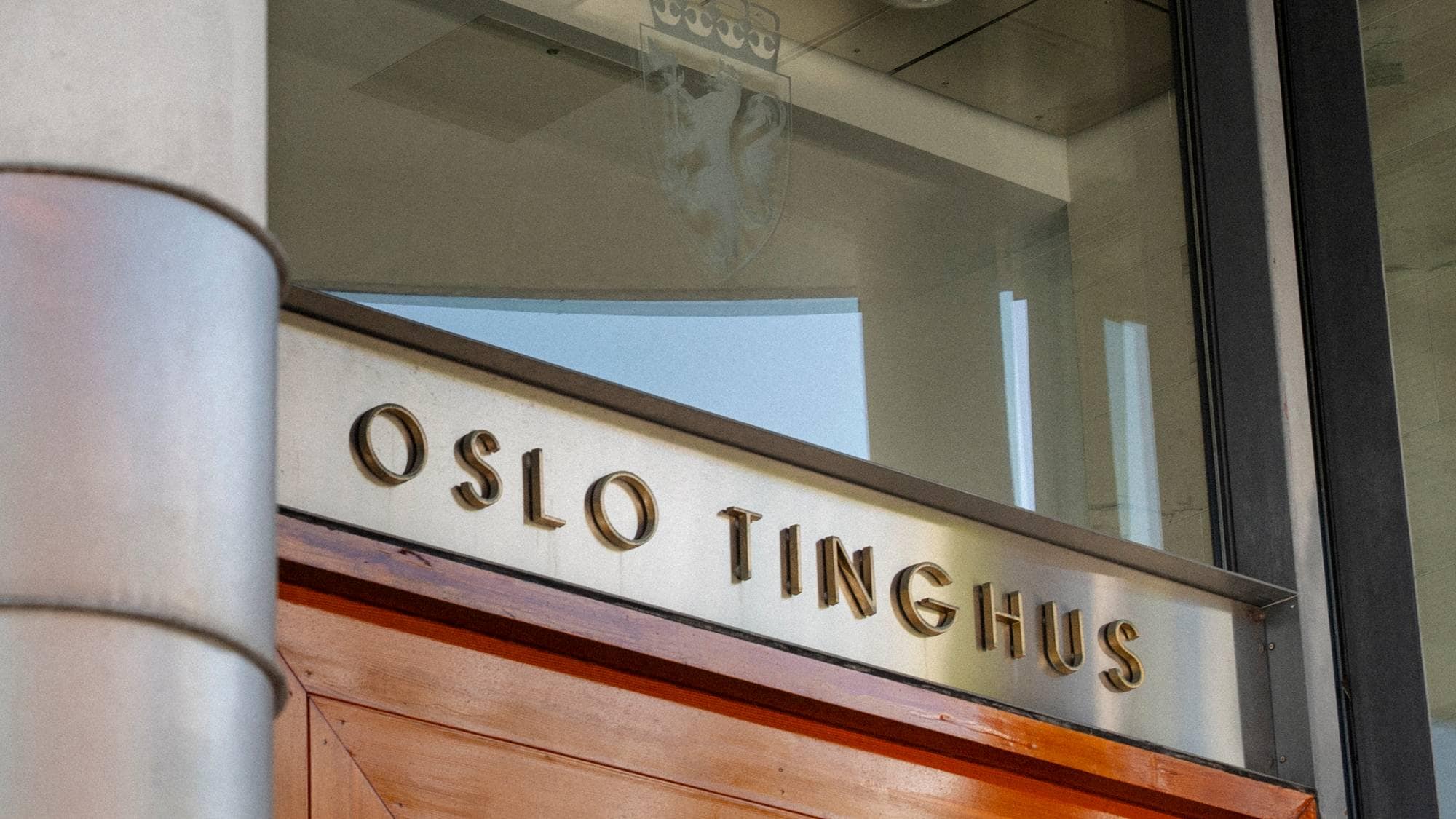Et skilt med teksten "Oslo tinghus" er montert over en tredør. Et riksvåpen er synlig i vinduet over skiltet. Bildet er tatt nært inngangspartiet til bygget. (Bildebeskrivelsen er laget av en KI-tjeneste)
