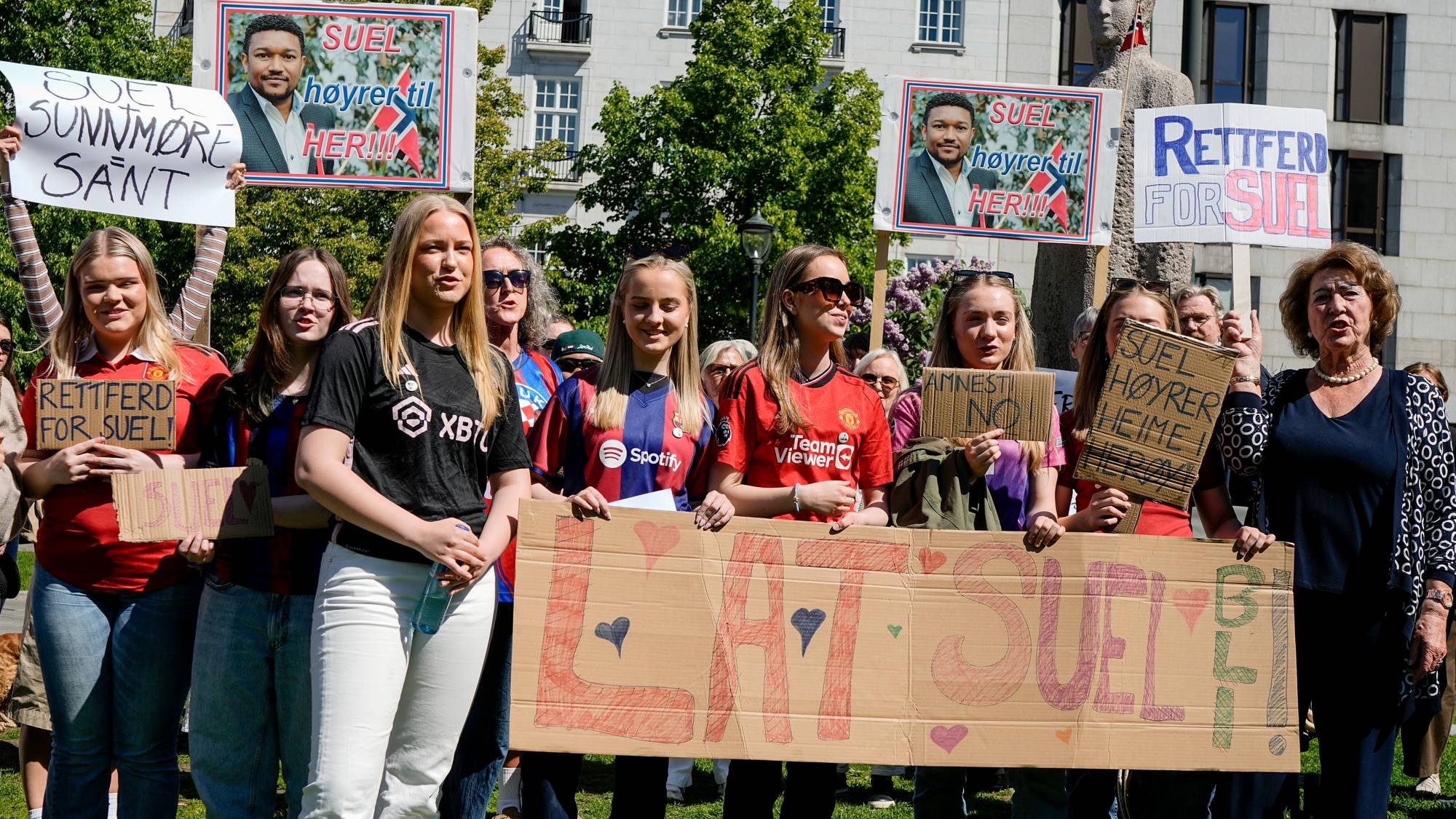 En gruppe mennesker demonstrerer utendørs. De holder opp skilt med påskriftene "Rettferd for Suel" og "Suel høyrer til heime". En av plakatene viser et bilde av en mann. Bygninger ses i bakgrunnen. (Bildebeskrivelsen er laget av en KI-tjeneste)