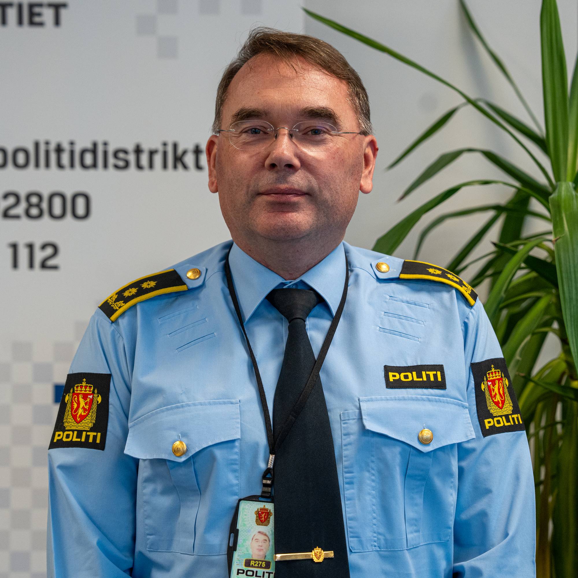 Politiansatt i uniform foran Øst politidistrikt sin logo. (Bildebeskrivelsen er laget av en KI-tjeneste)