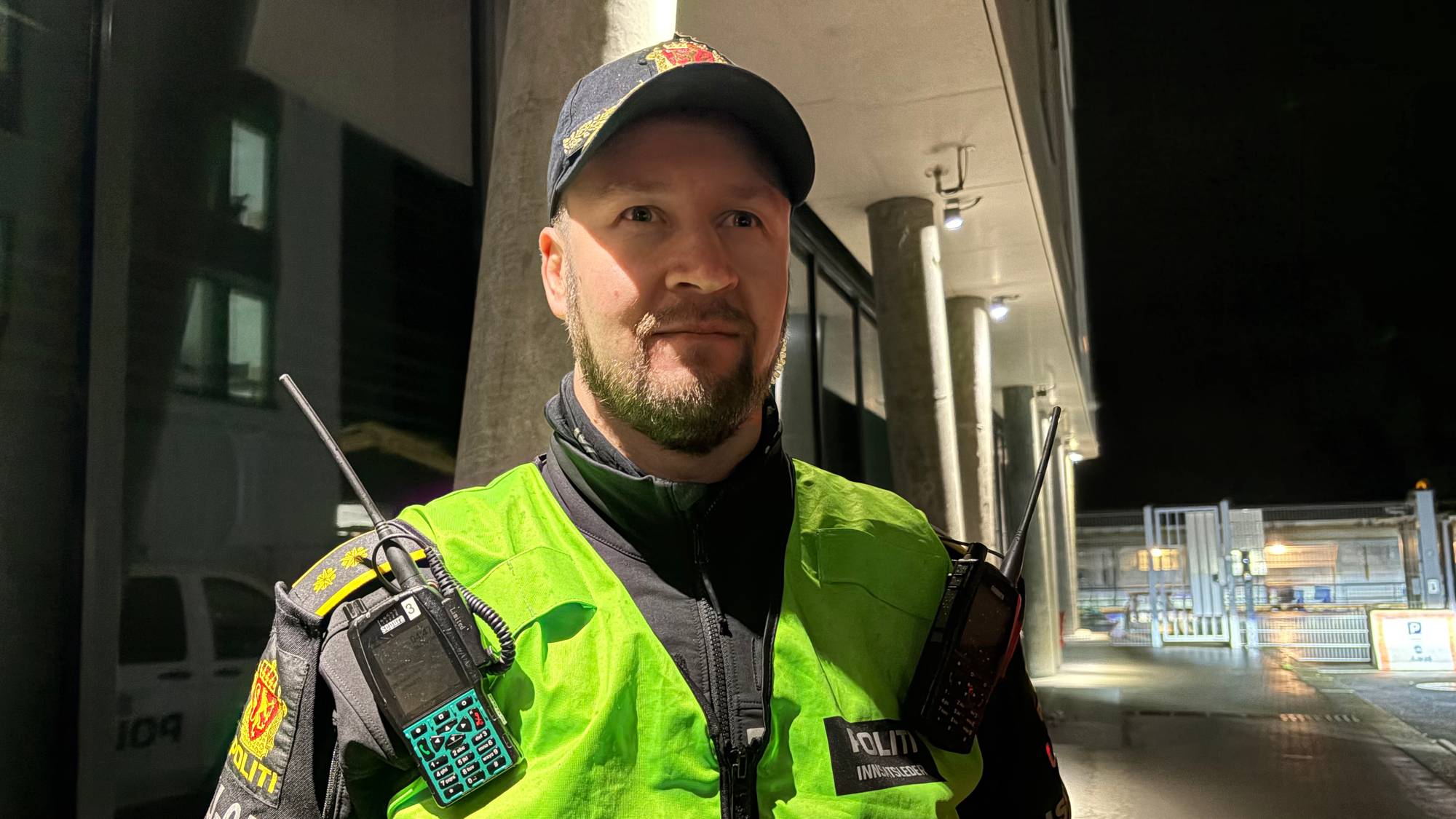 Politioverbetjent i uniform står utendørs om kvelden. Han har på seg gul refleksvest med sambandsutstyr. (Bildebeskrivelsen er laget av en KI-tjeneste)