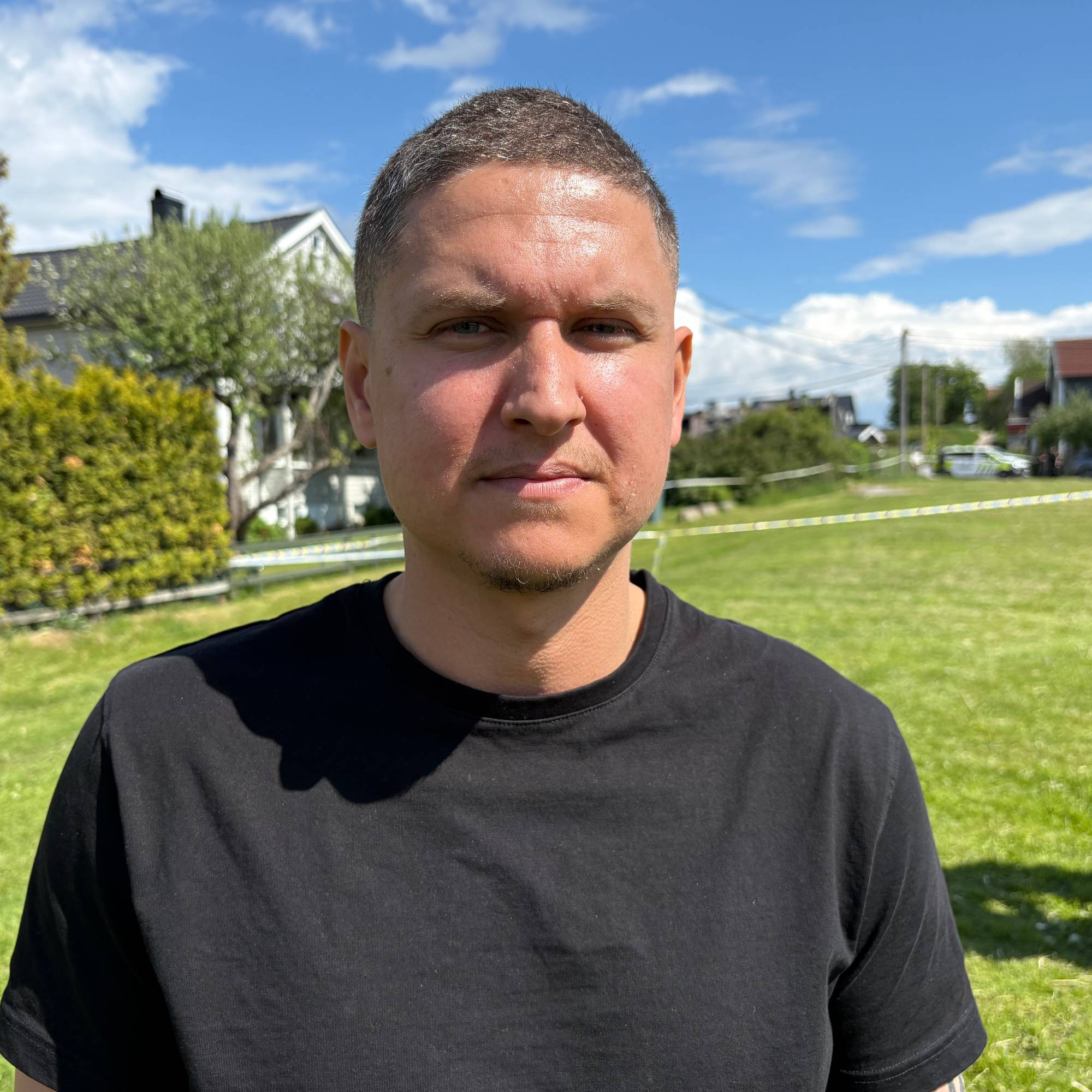 En mann i svart t-skjorte står foran et grønt gressfelt. 
