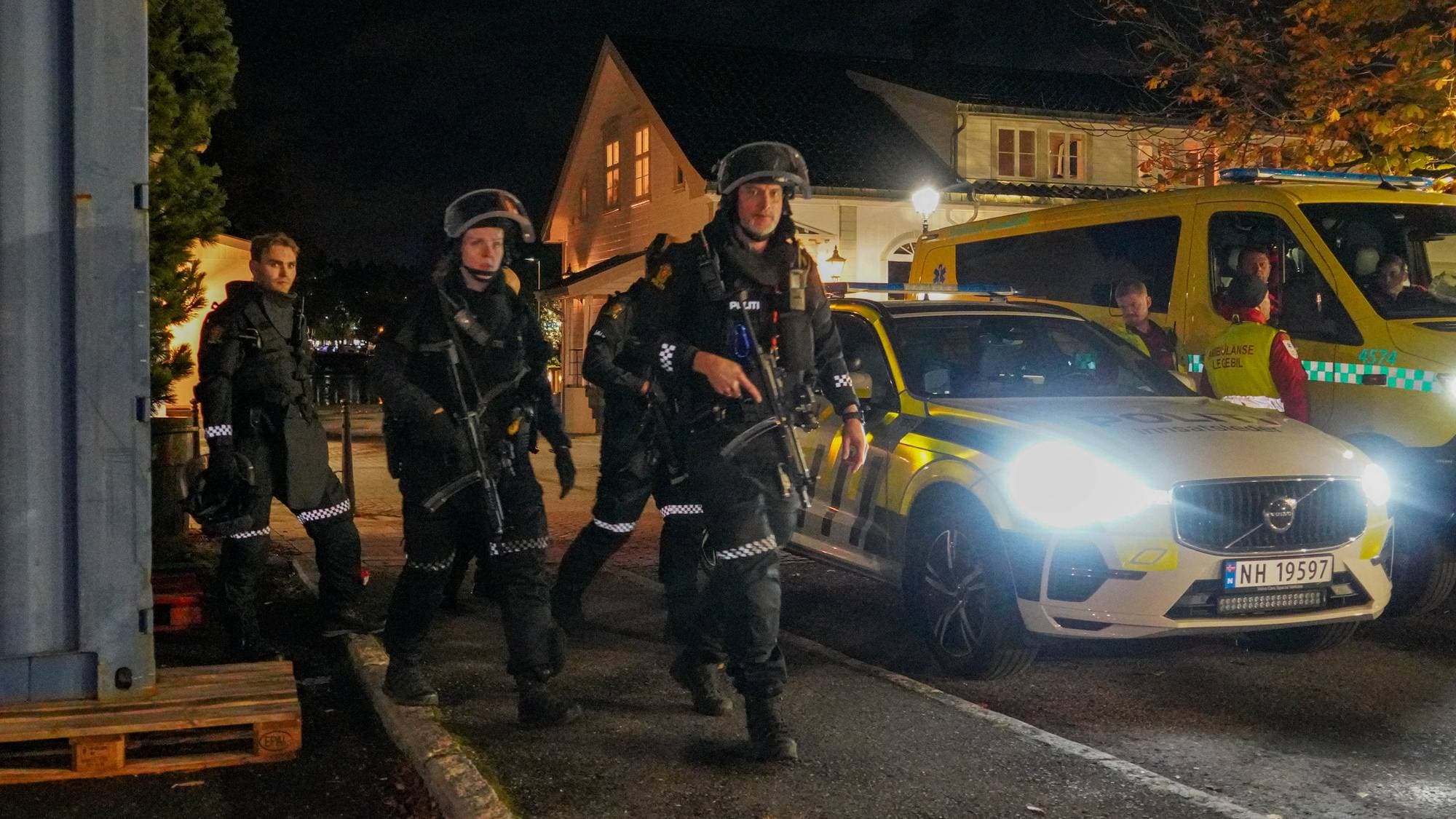 Bevæpnet politi i uniform ved en politibil og ambulanse om natten. (Bildebeskrivelsen er laget av en KI-tjeneste)