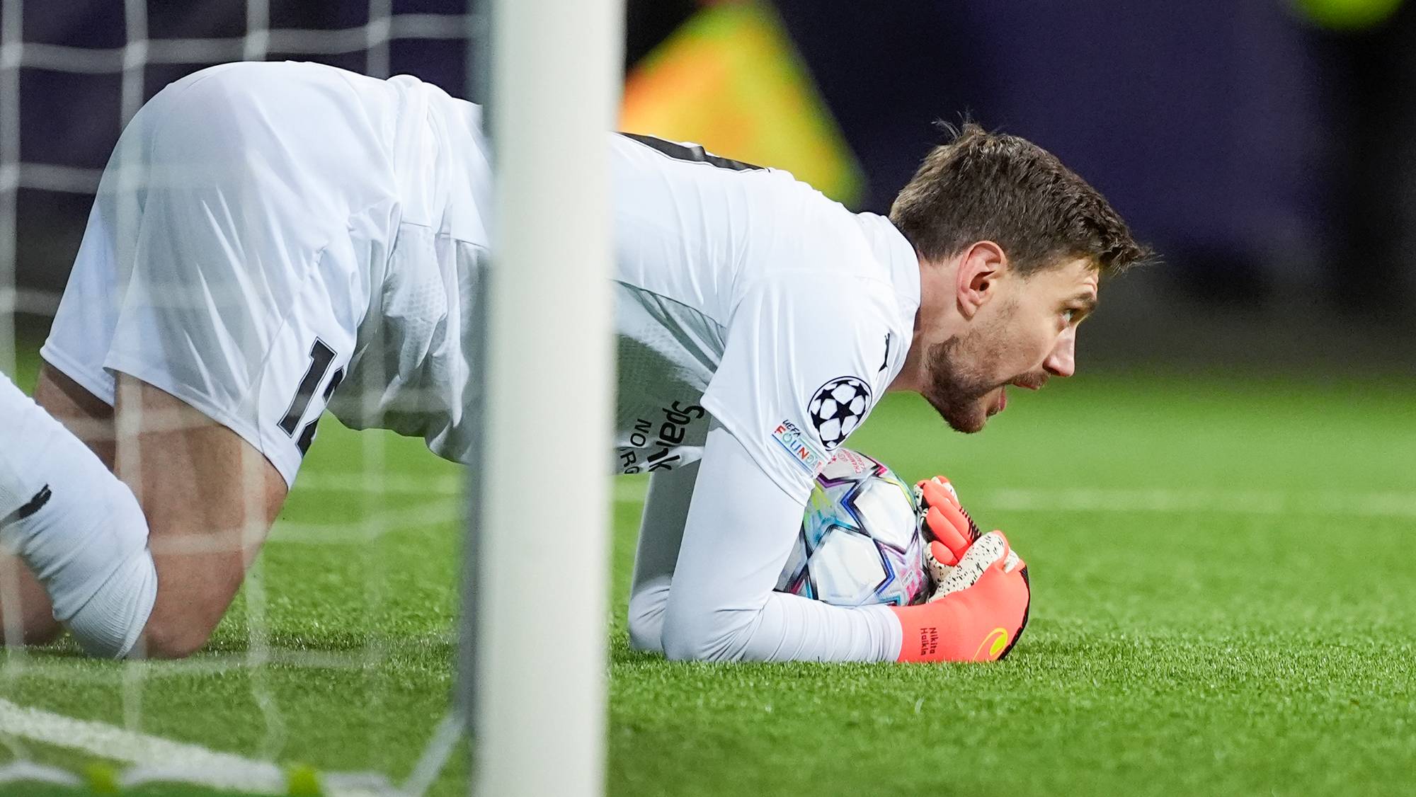 Keeper ligger på knærne og holder ballen foran mål på en fotballbane. (Bildebeskrivelsen er laget av en KI-tjeneste)