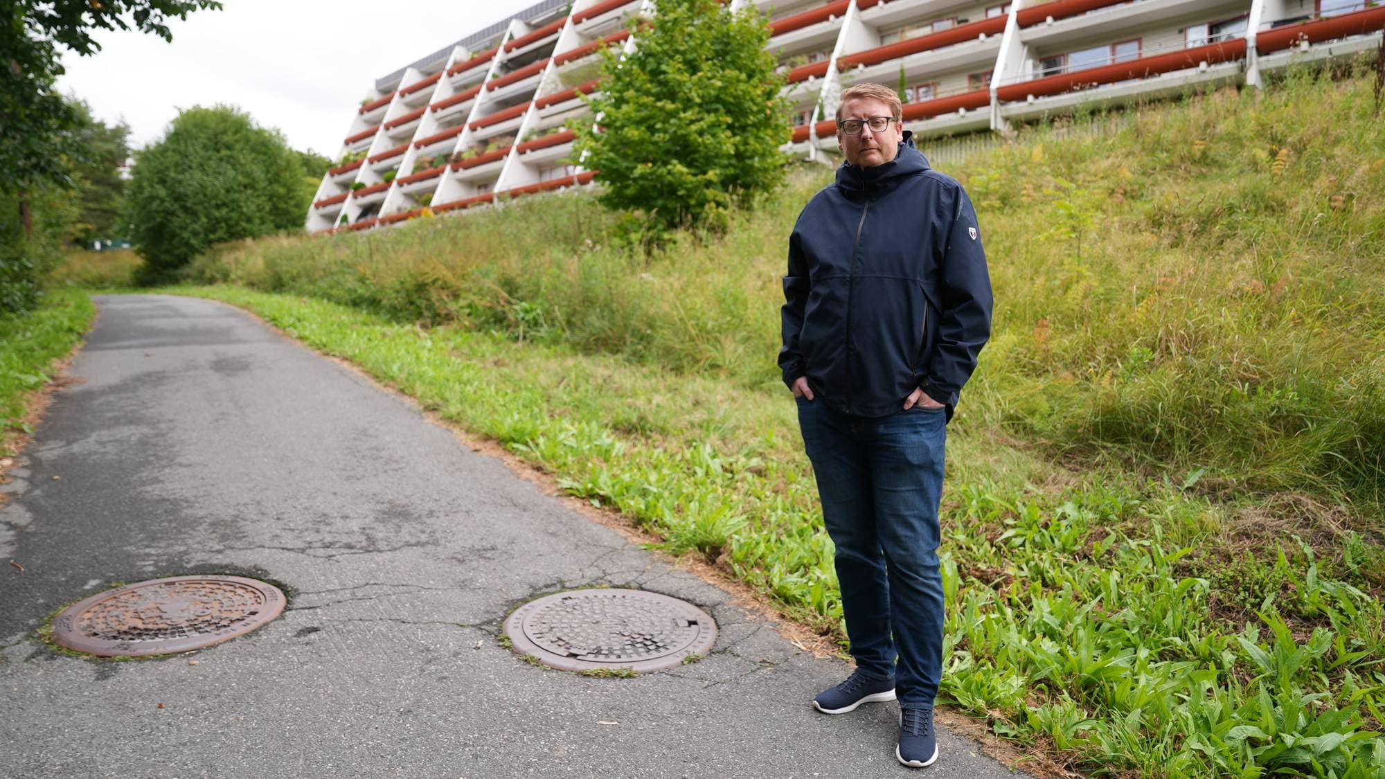 Mann står på en vei ved et boligkompleks. (Bildebeskrivelsen er laget av en KI-tjeneste)