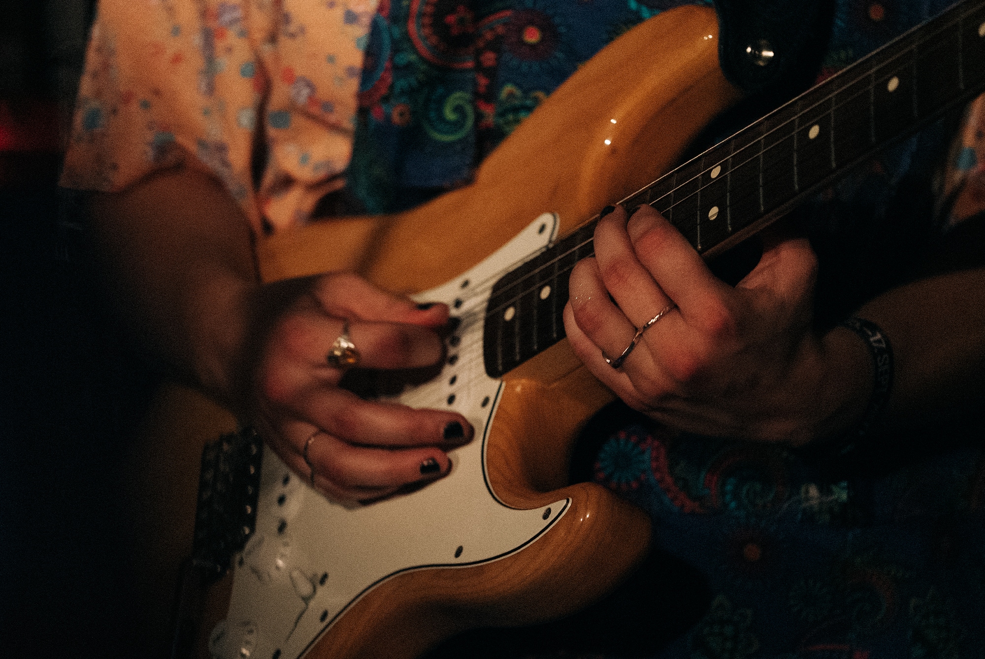 Nærbilde av el-gitaren med Mie som spiller på den. Mie har neglelakk og flere ringer. 
