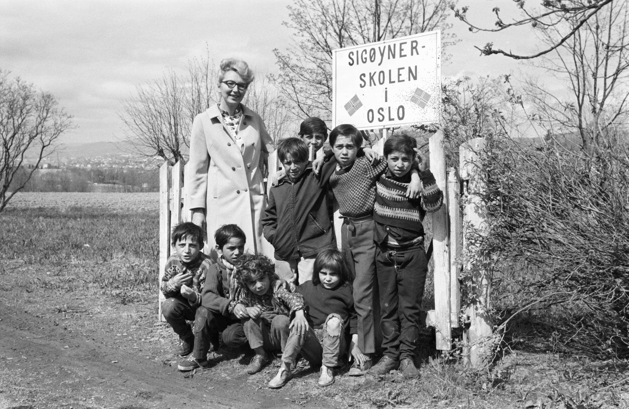 Lærer Unn Jørstad sammen med flere romske barn. De står foran et skilt der det står "Sigøynerskolen i Oslo". 