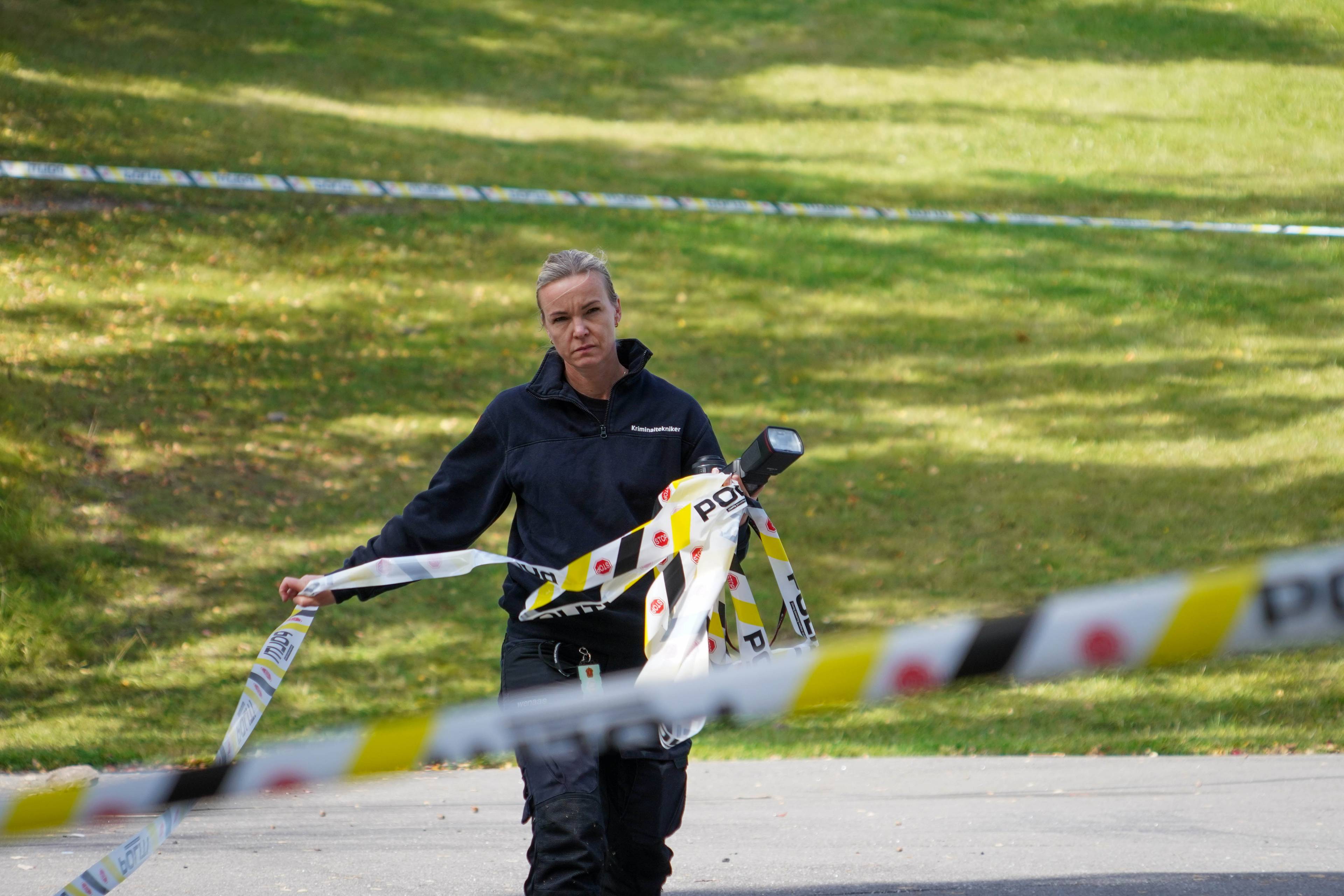 En person bærer en gjenstand surret inn i politi-tape inne på et område sperret av med politi-tape.