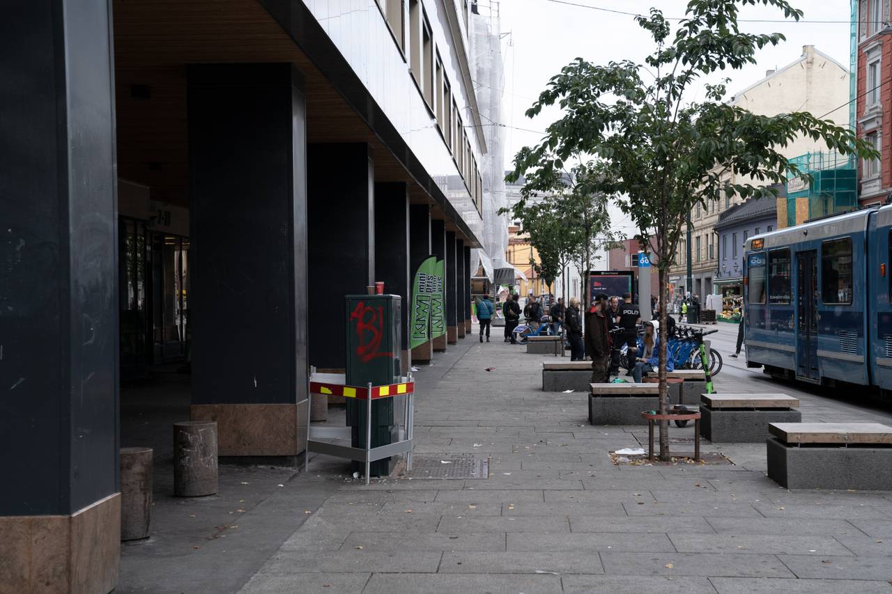 Bildet viser rusbrukere i det åpne rusmiljøet i Storgata i Oslo. På bildet ser vi også at politiet og utekontakter er til stede. På bildet ser man også bysykler og i bakgrunnen er det bygårder og butikker.