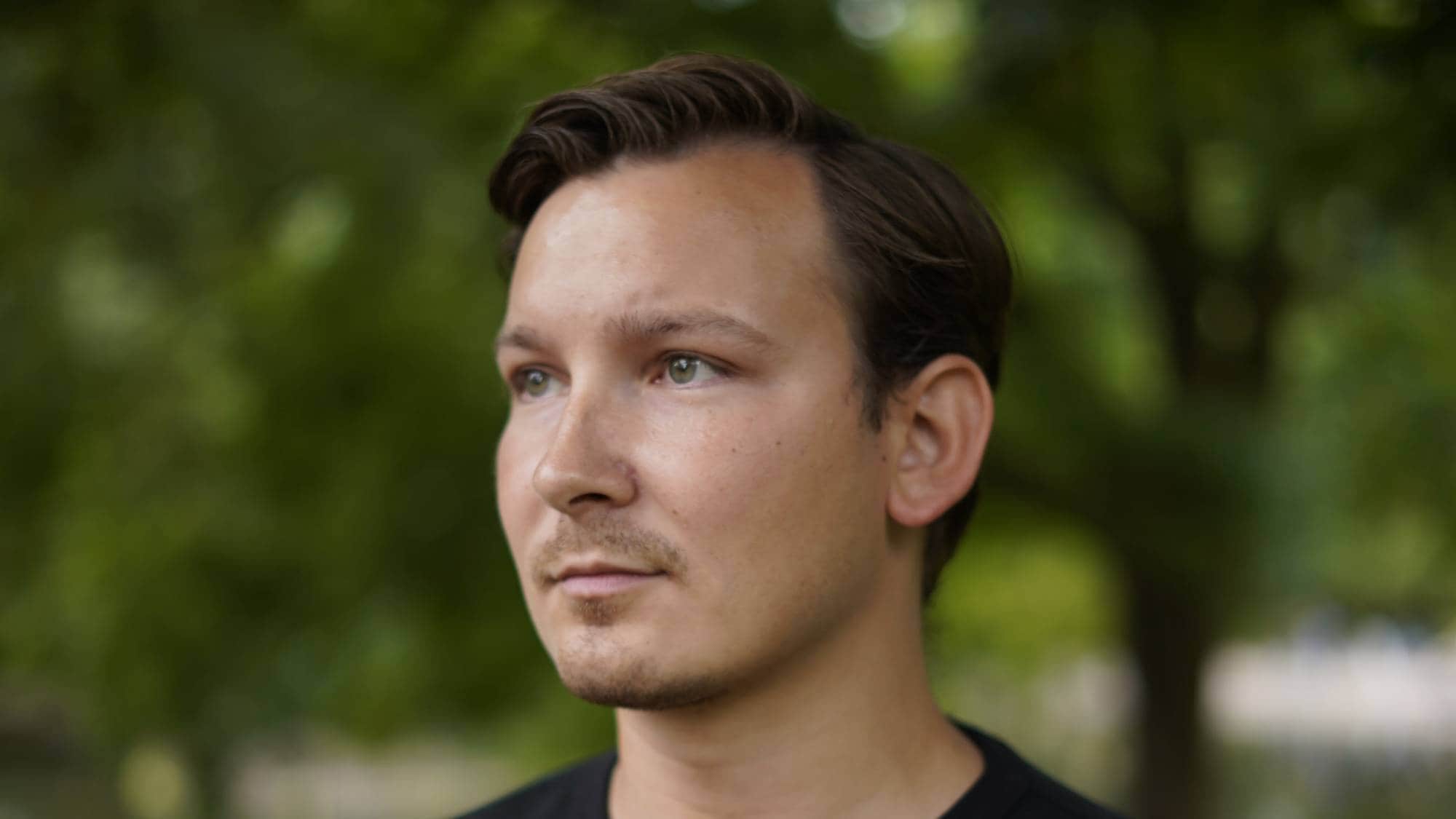 En ung mann mørkeblå genser står ute i Slottsparken og ser litt forbi kameraet