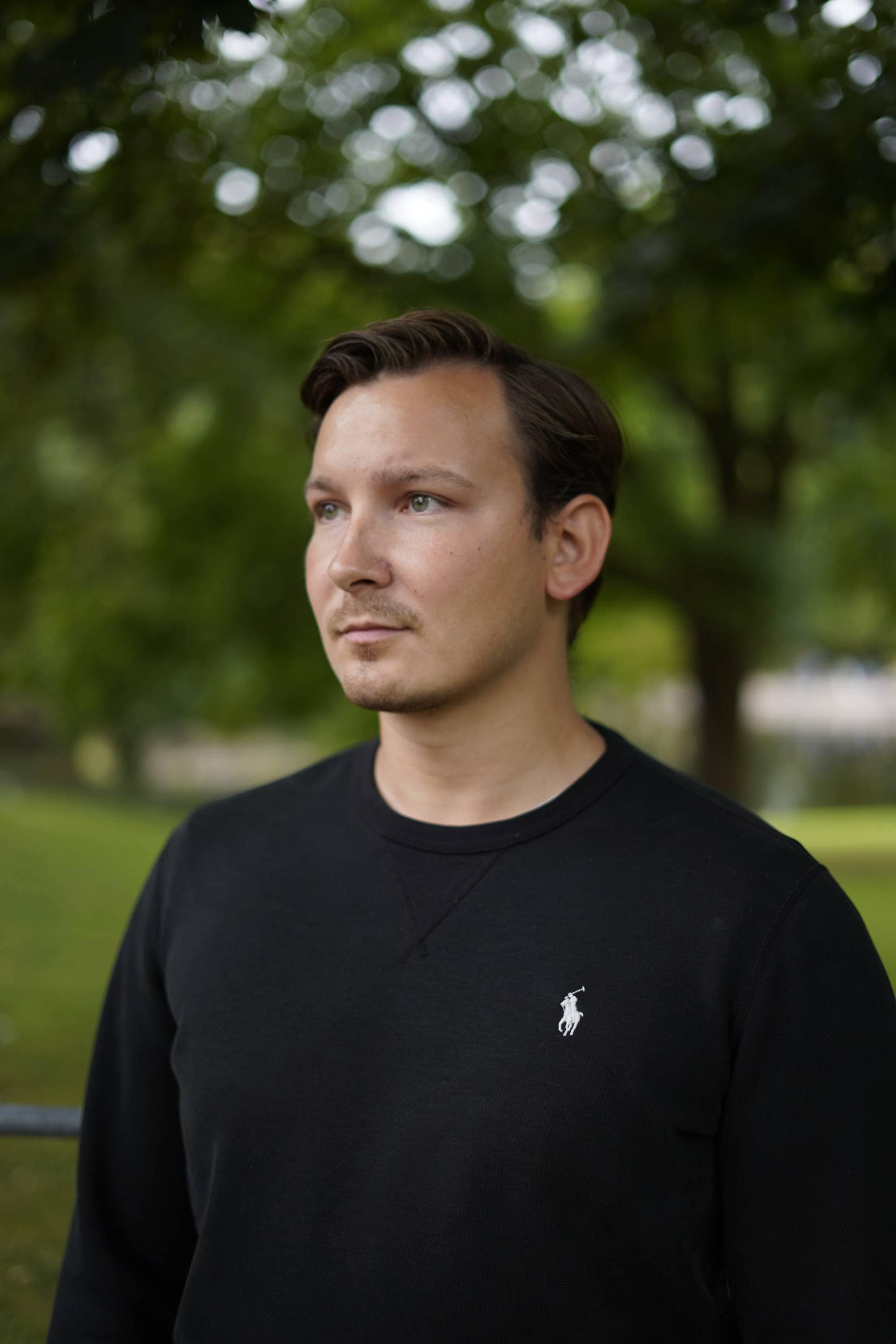En ung mann mørkeblå genser står ute i Slottsparken og ser litt forbi kameraet