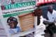 Sodiq Adelakun / Reuters / NTB En person holder opp avisen "The Nation," som viser en artikkel om Nigeria og USA som rammer terrorister i Nordvest. Avisens forside inneholder en stor overskrift og delvis tekst på et håndskrevet papir. I bakgrunnen sitter en annen person med en avis i hånden. Omgivelsene ser ut til å være et utendørs område med avissalg. (Bildebeskrivelsen er laget av en KI-tjeneste)