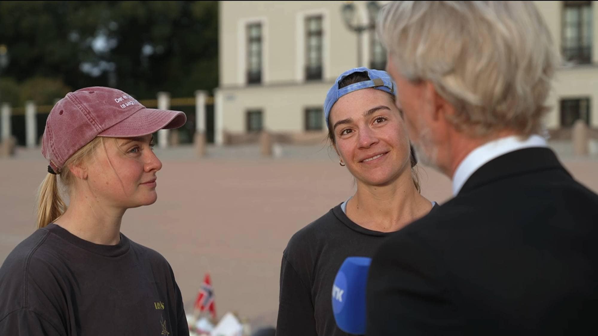 To kvinner blir intervjuet av en journalist foran Det kongelige slott. (Bildebeskrivelsen er laget av en KI-tjeneste)
