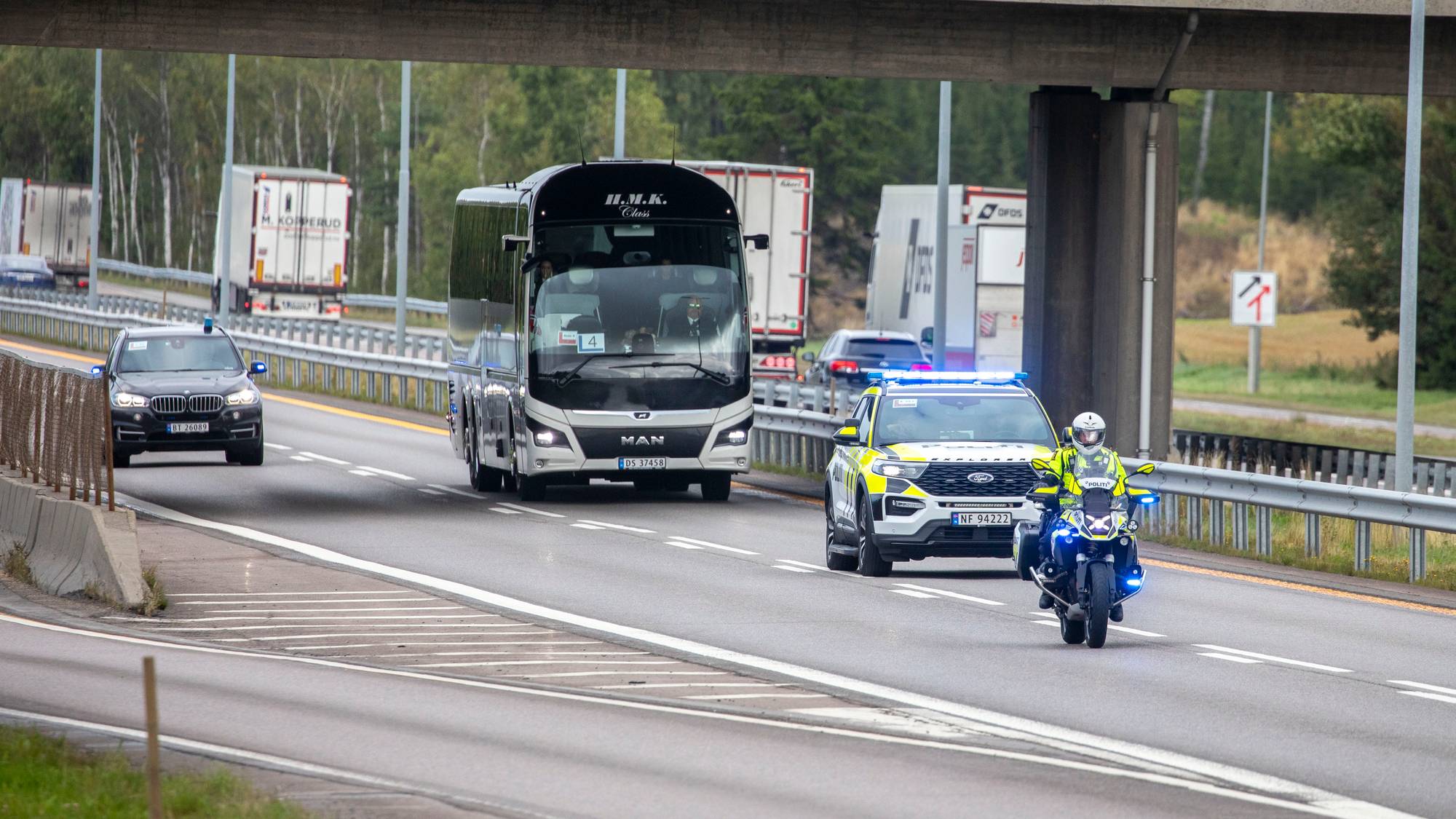 Politibil og motorsykkel eskorterer en turbuss på motorvei. (Bildebeskrivelsen er laget av en KI-tjeneste)