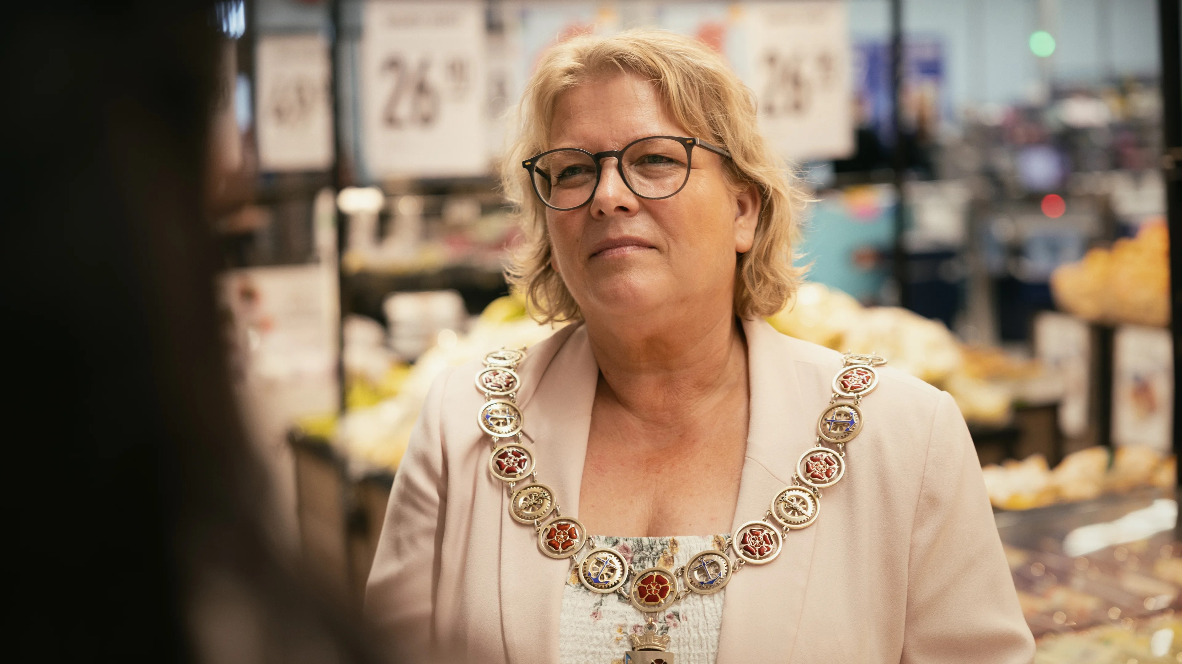 en kvinne med skulderlangt lyst hår og briller . Hun har på seg et ordførerkjede