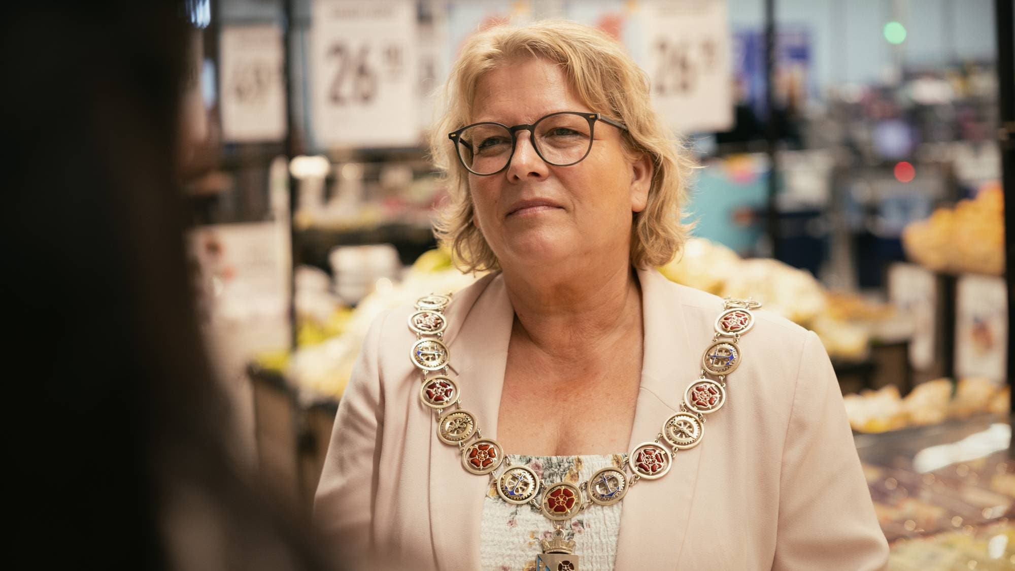 en kvinne med skulderlangt lyst hår og briller . Hun har på seg et ordførerkjede