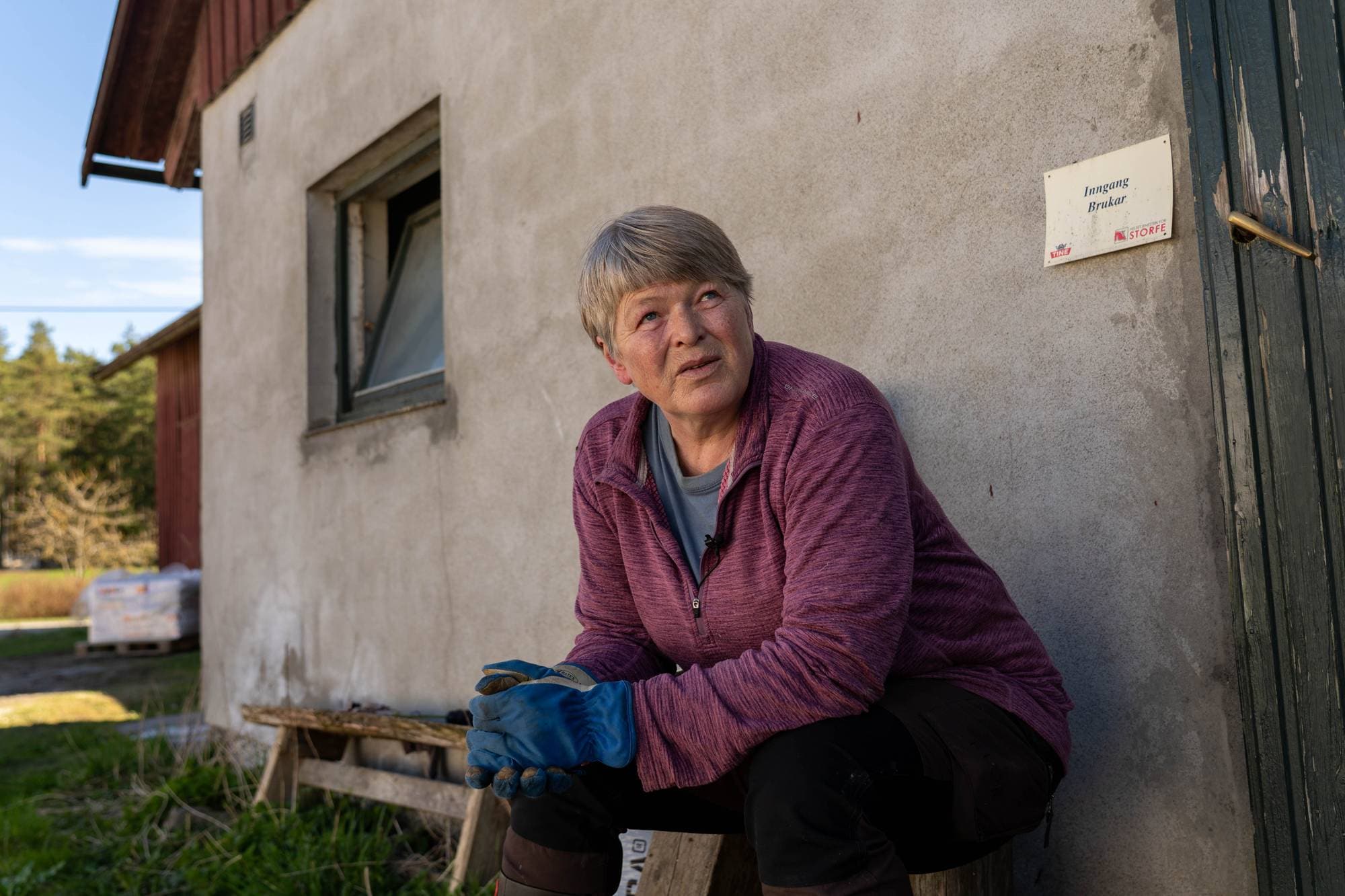 Bonde Eva Skår Sørli sitter på en benk utenfor fjøset sitt. 