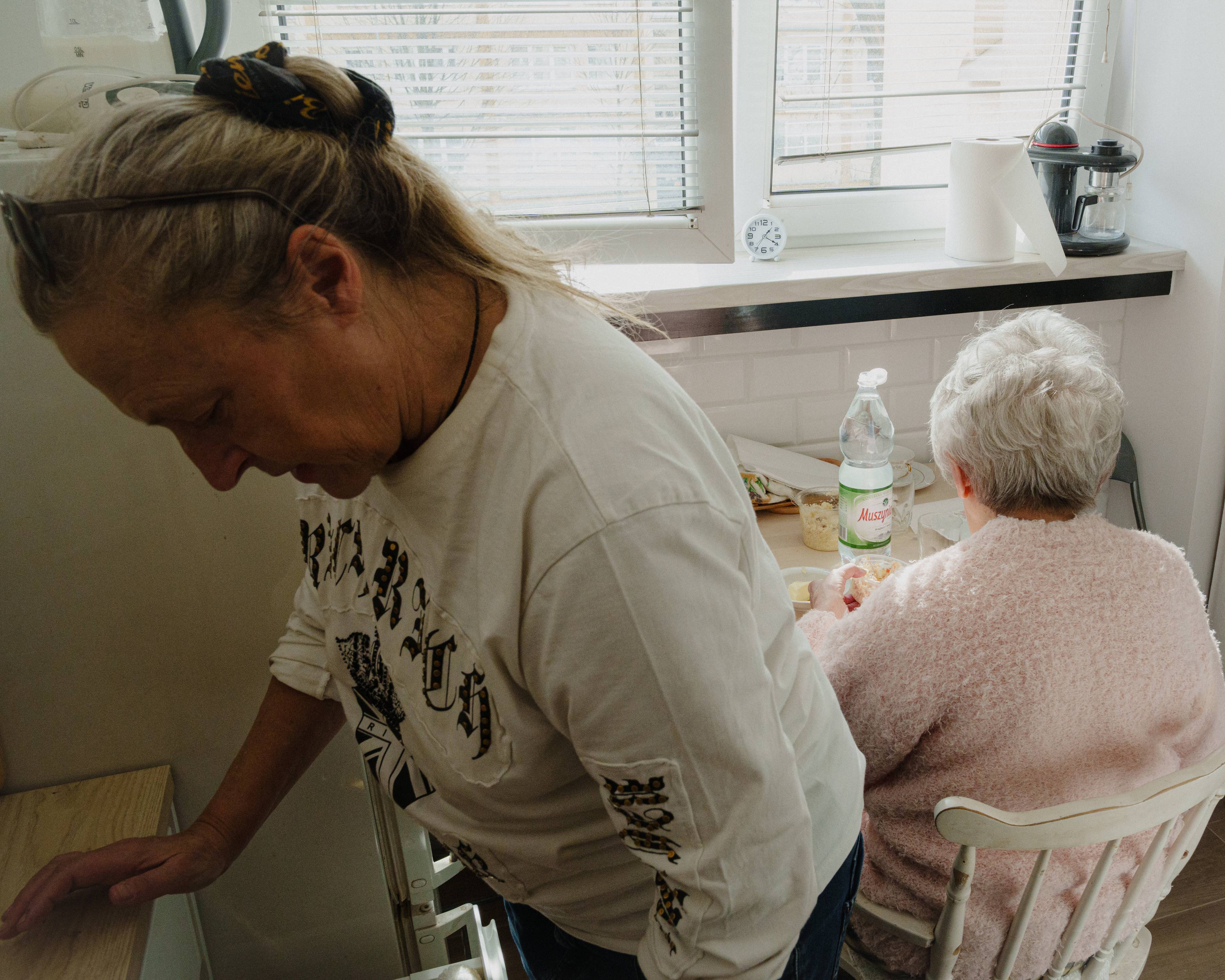 Edith gjør noe på kjøkkenet mens Magdalena sitter ved bordet litt lenger bortenfor