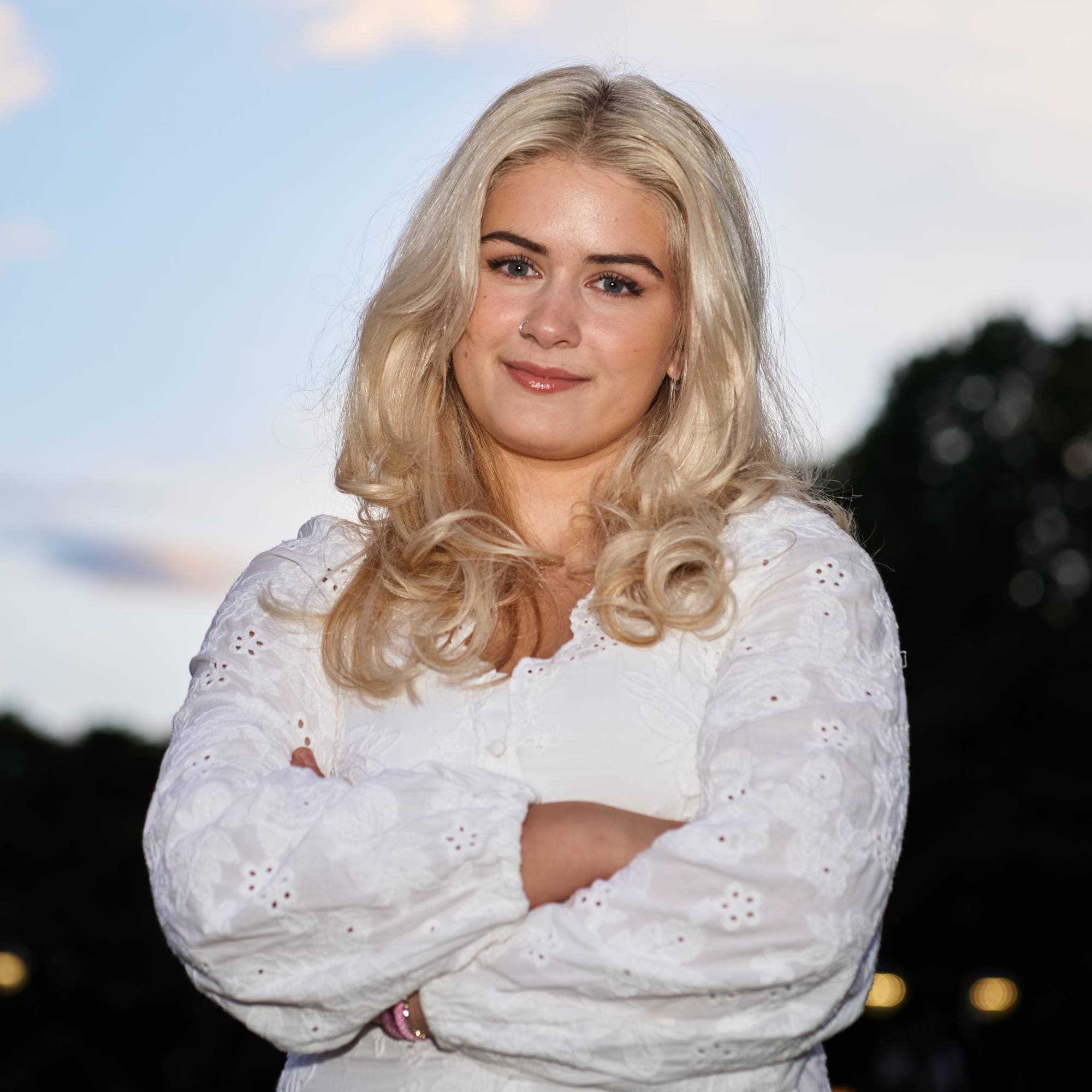 Portrett av en blond kvinne med armene i kors, iført en hvit bluse med blonder. (Bildebeskrivelsen er laget av en KI-tjeneste)