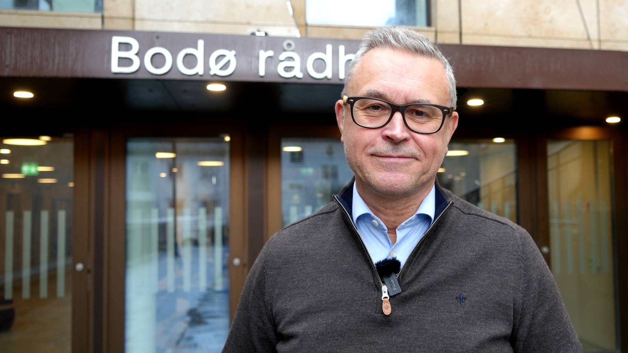 En mann med grått hår og briller står foran Bodø Rådhus. 
