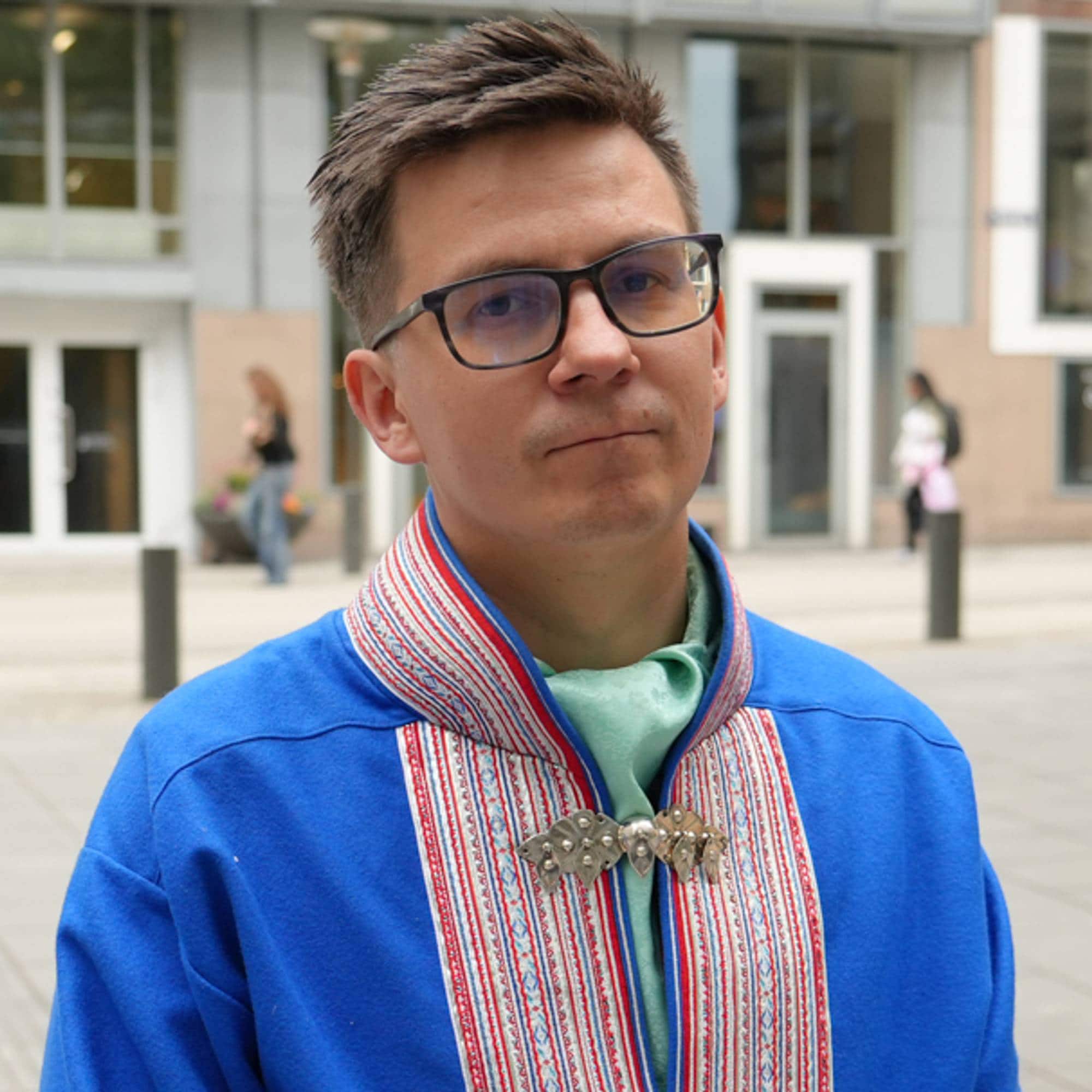 Mann iført blå kofte står utendørs foran en kontorbygning i Oslo sentrum. (Bildebeskrivelsen er laget av en KI-tjeneste)